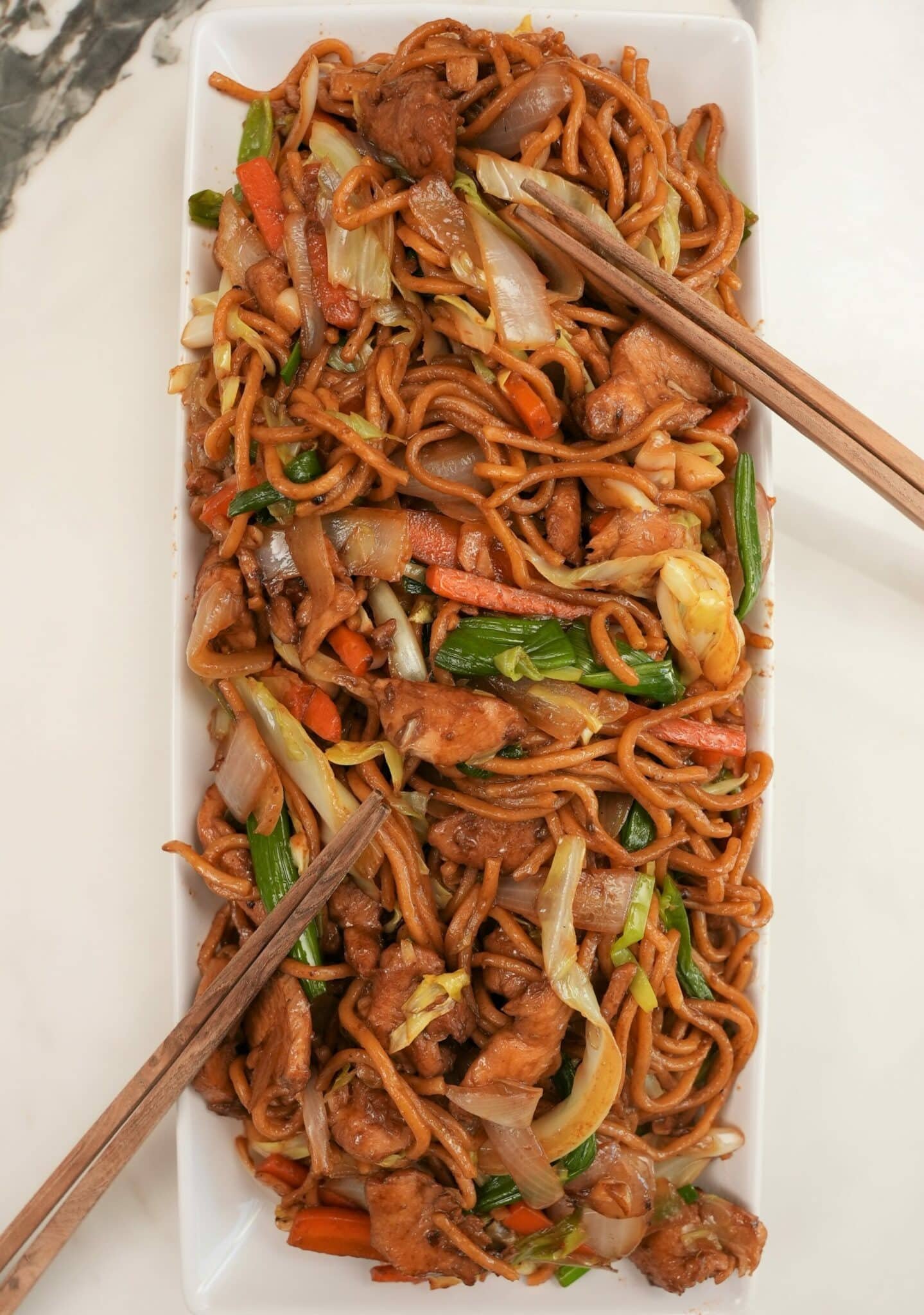 A photo of Chicken Lo Mein plated on a rectangular tray with chopsticks.