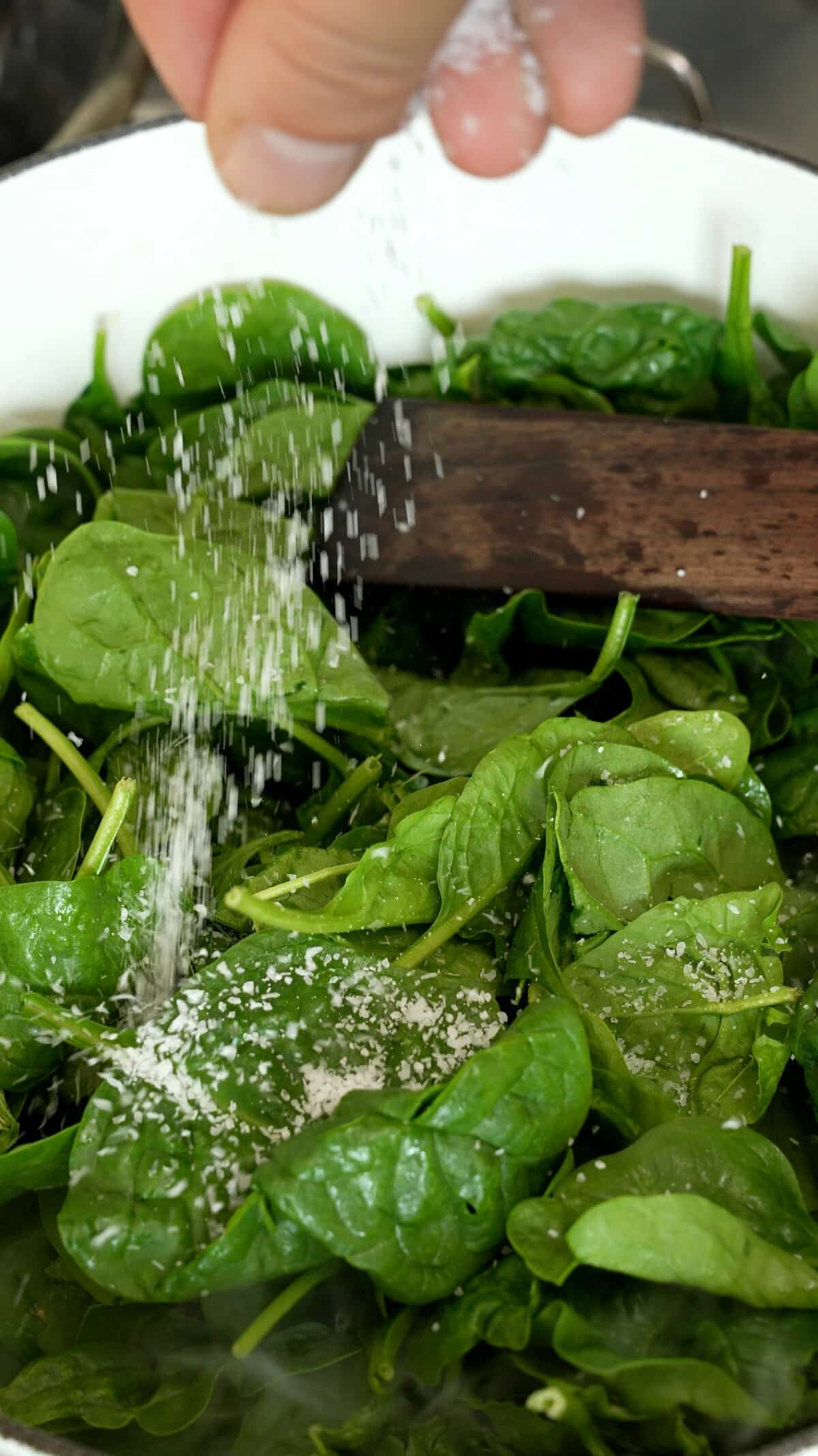 A hand salting spinach in a dutch oven.