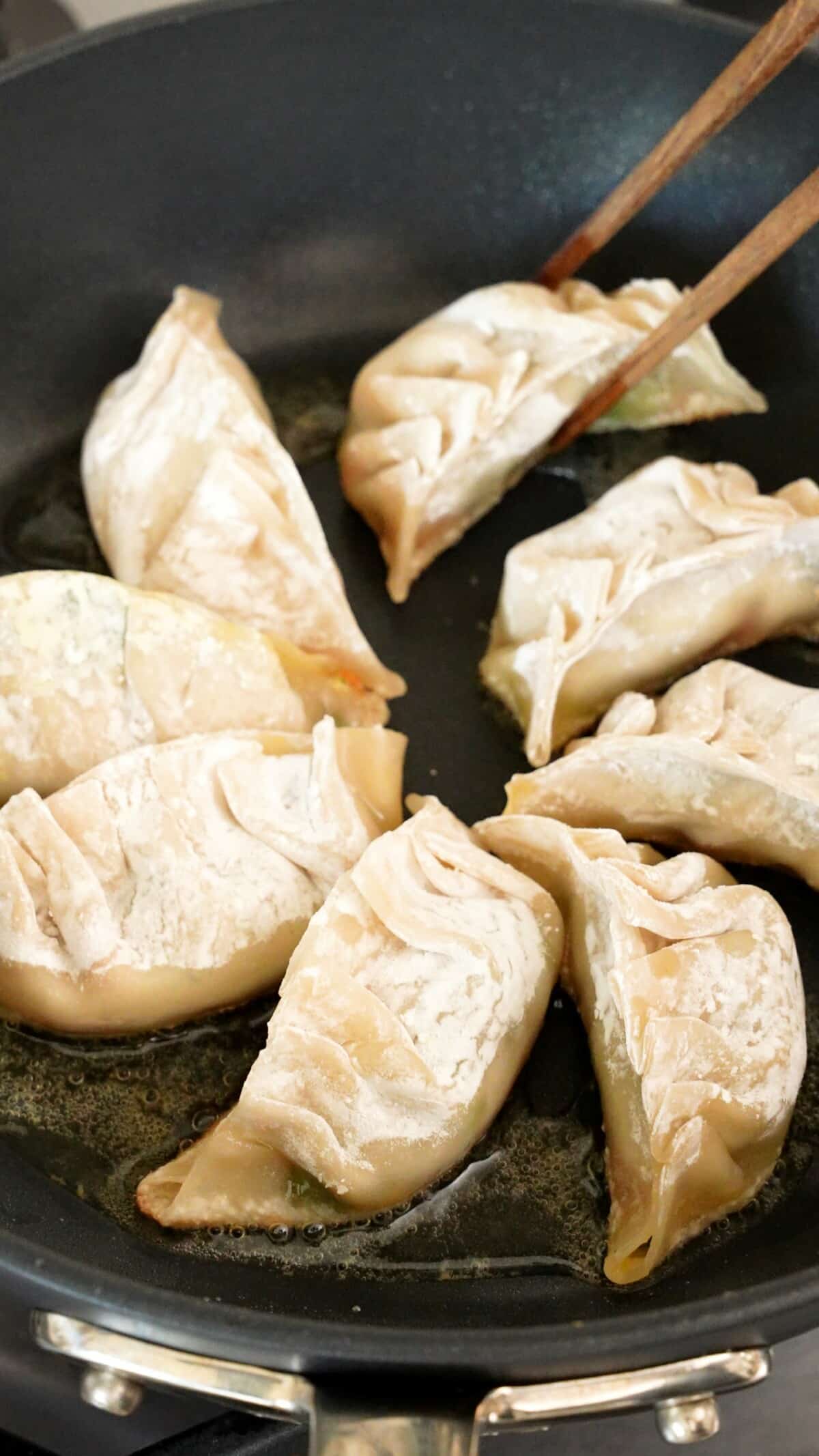 Fresh dumplings pan frying in a nonstick pan with neutral oil.