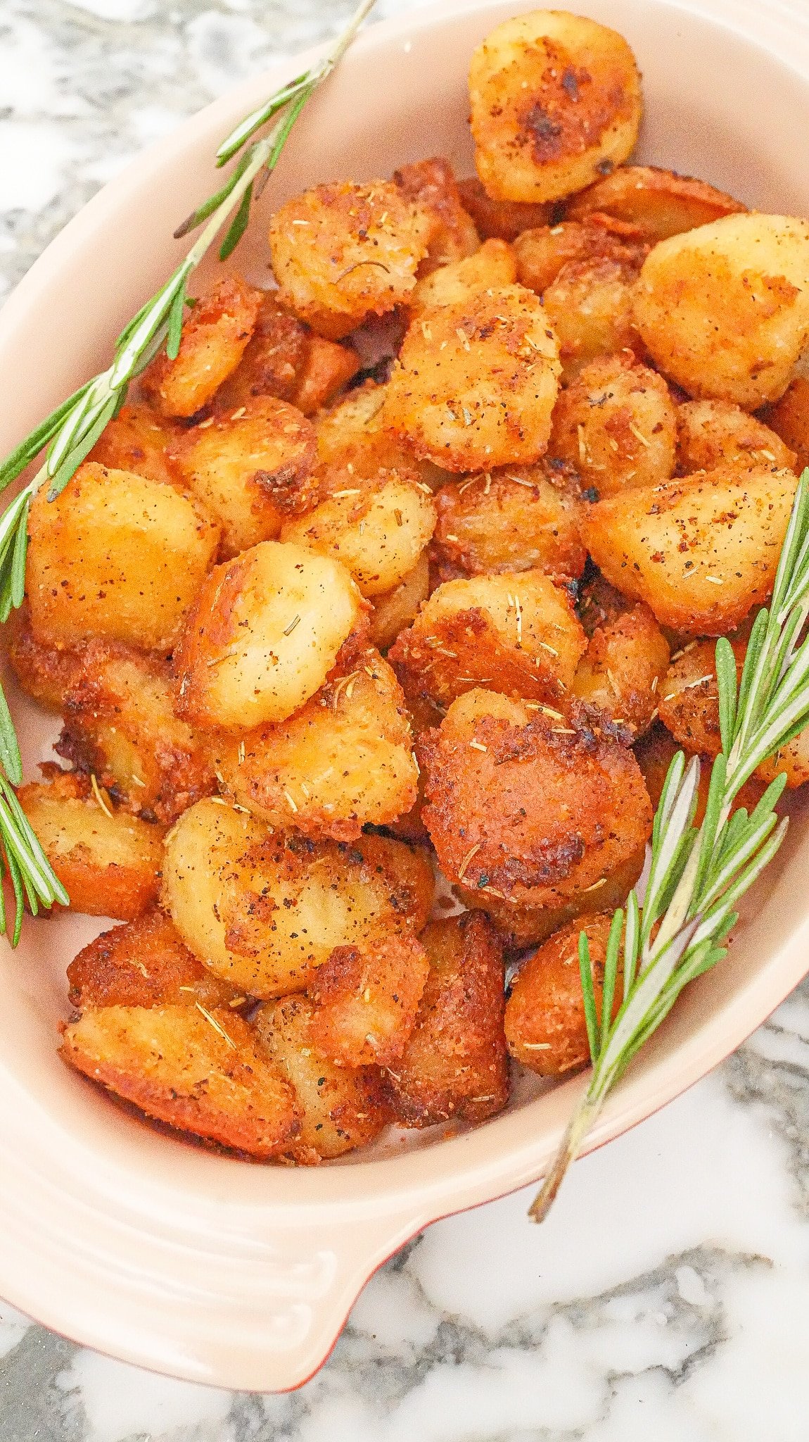 Crispy roasted potatoes in a serving dish with fresh rosemary sprigs.