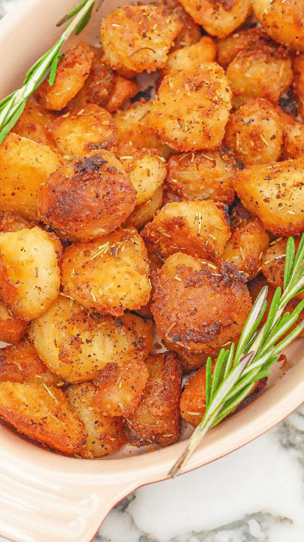 Crispy roasted potatoes in a tray with fresh rosemary.
