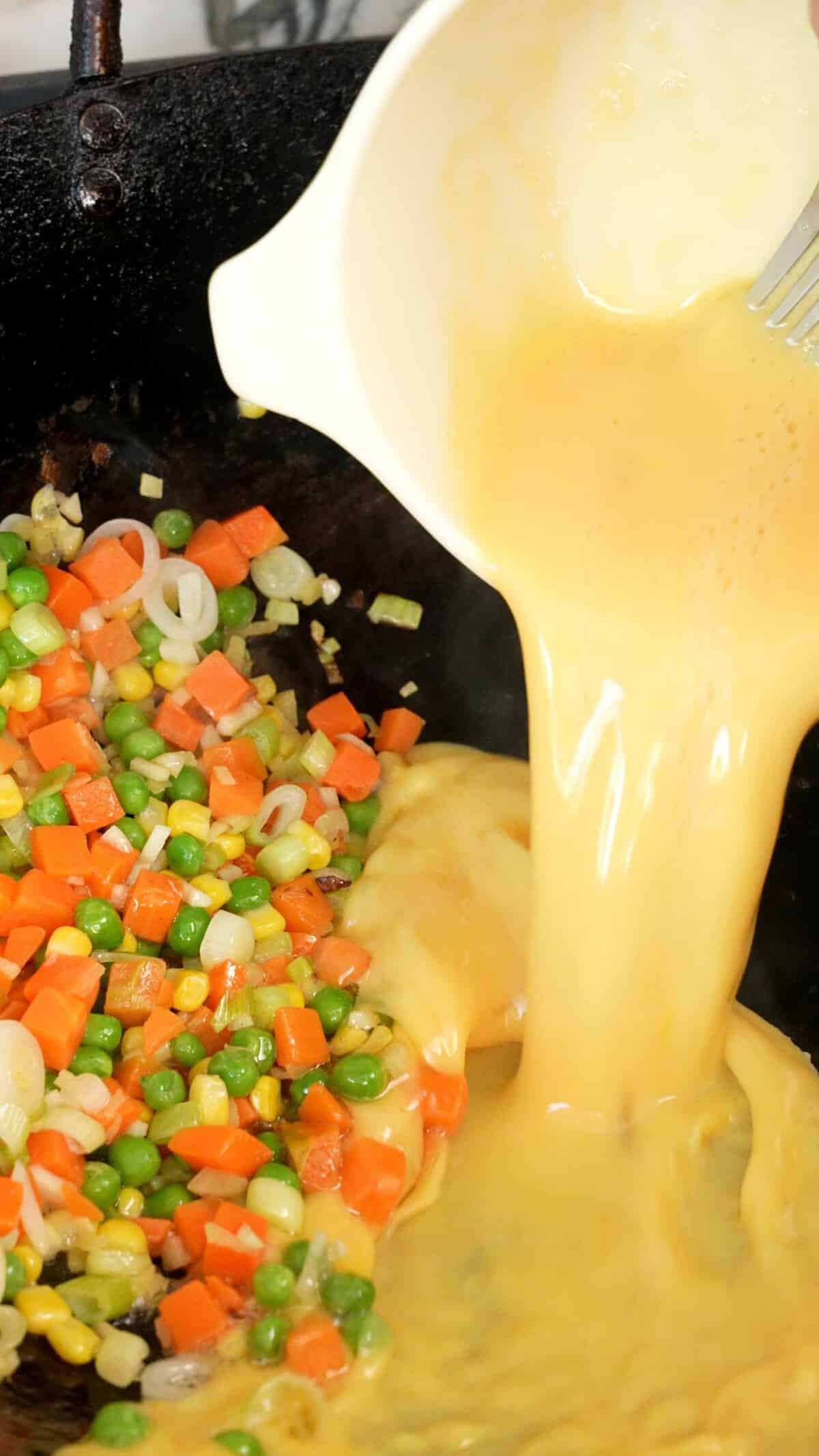 Pouring beaten egg into the wok with vegetables.