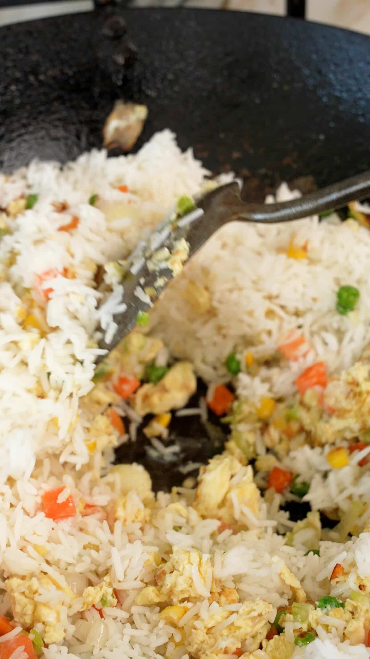 Adding day old white rice to the wok with eggs and vegetables.