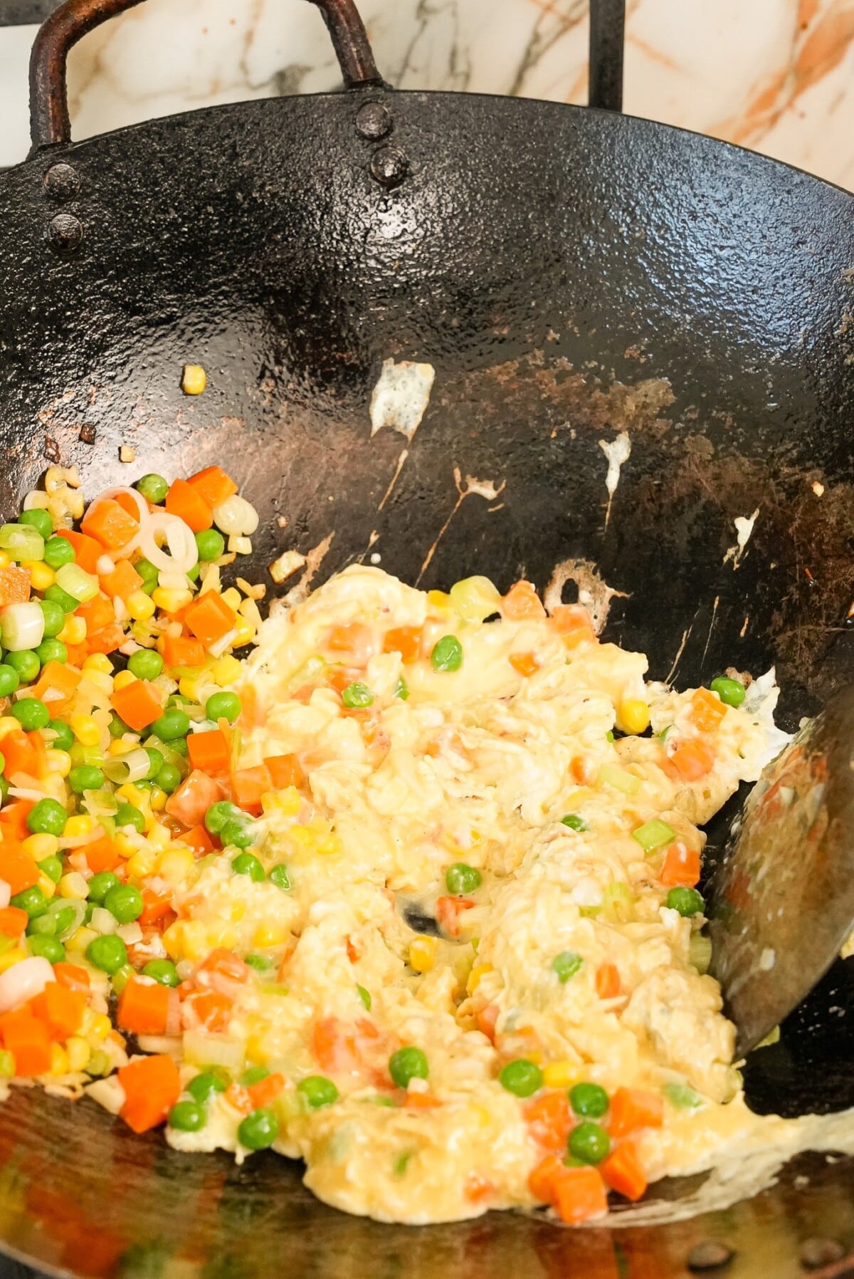 Scrambling egg in the wok with vegetables.