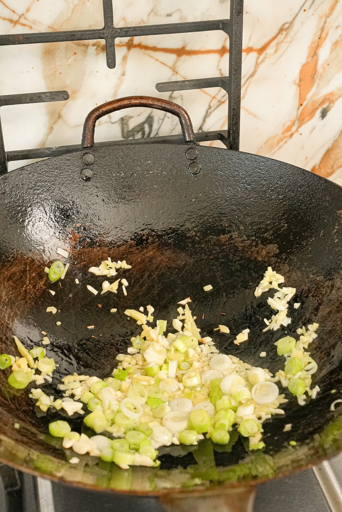 Frying scallions, garlic, and ginger, in a wok in neutral oil.