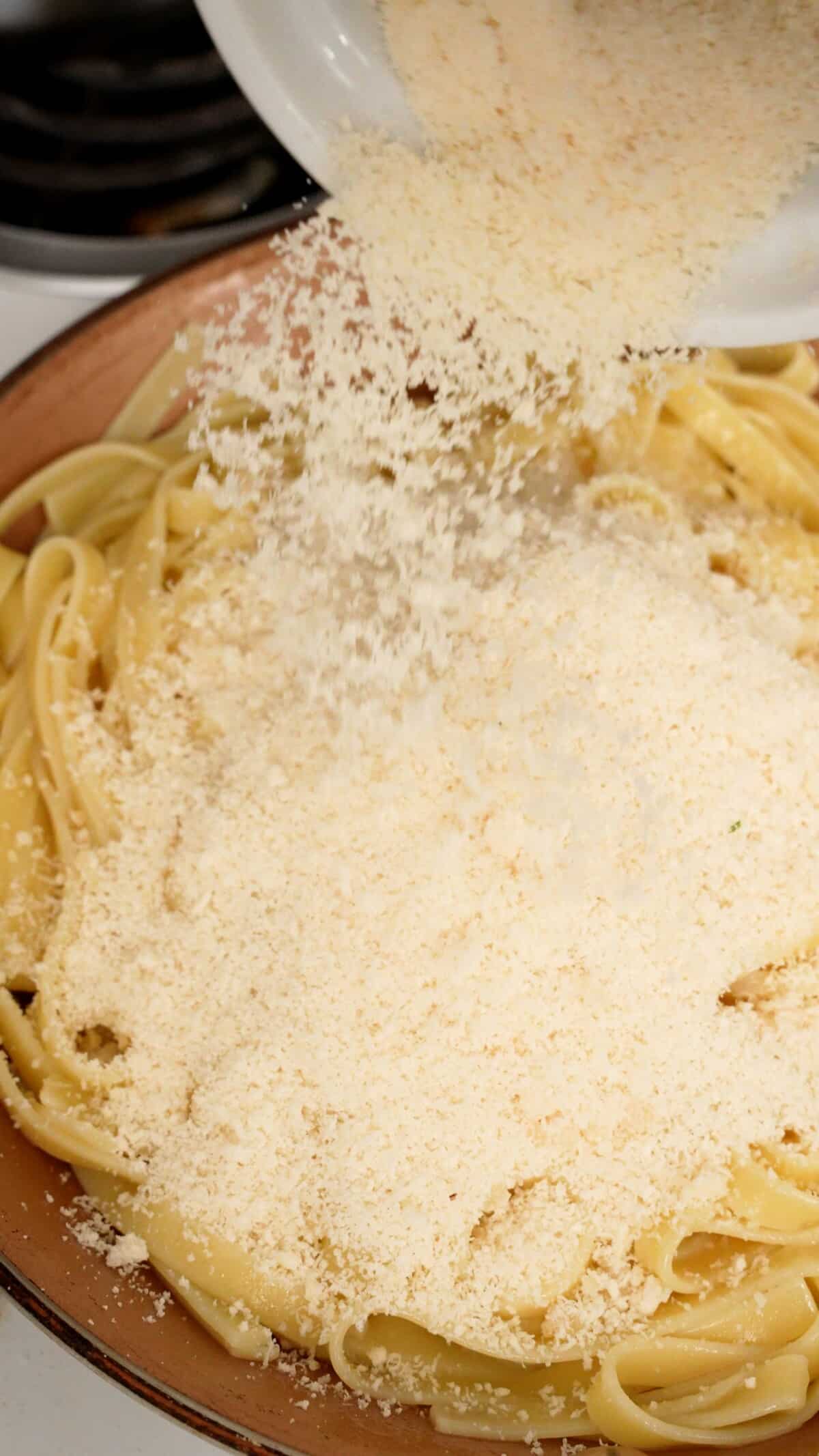 Parmesan cheese being added to pasta and butter in a pan.