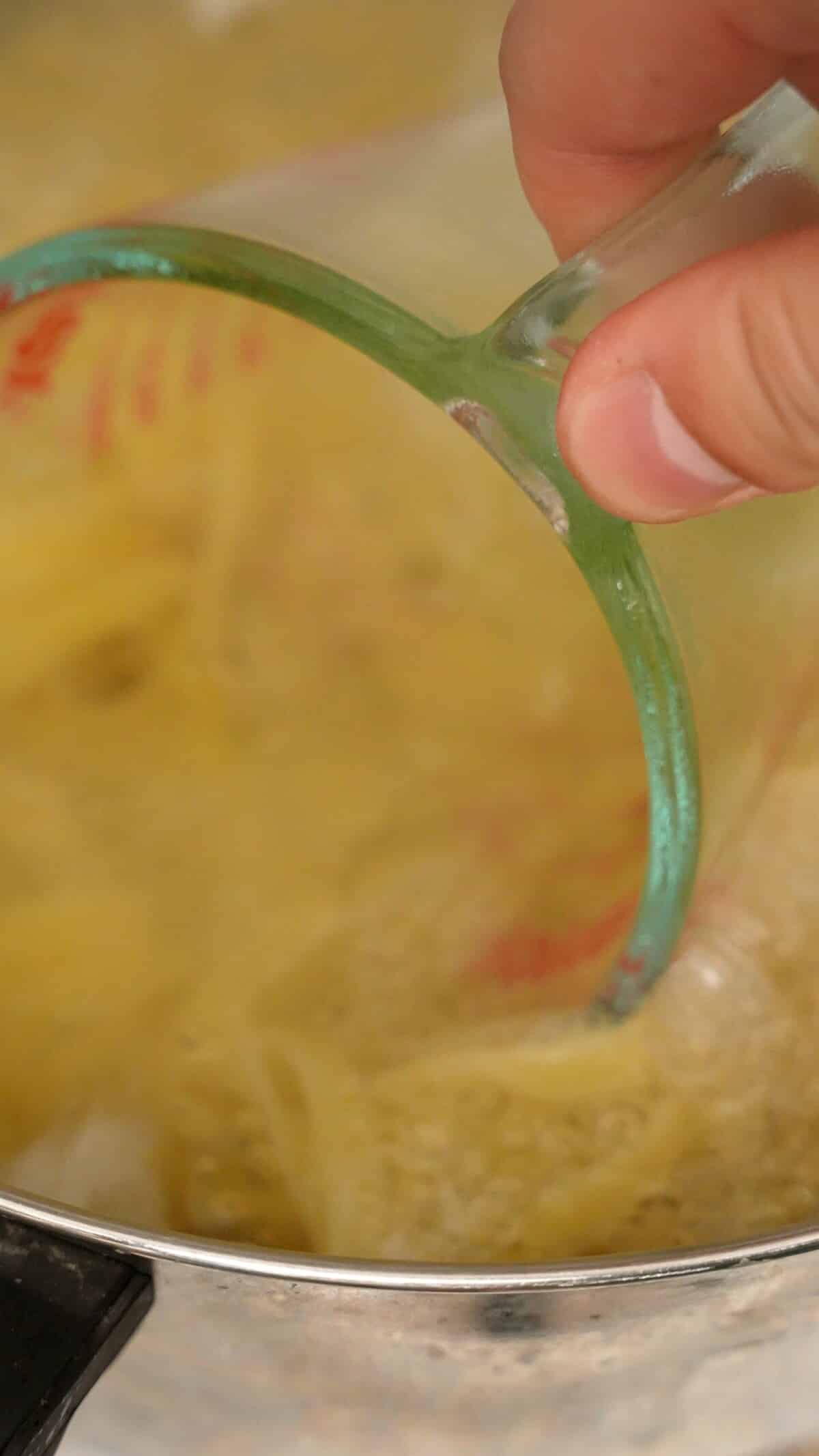 A measuring cup reserving pasta water from a pot.