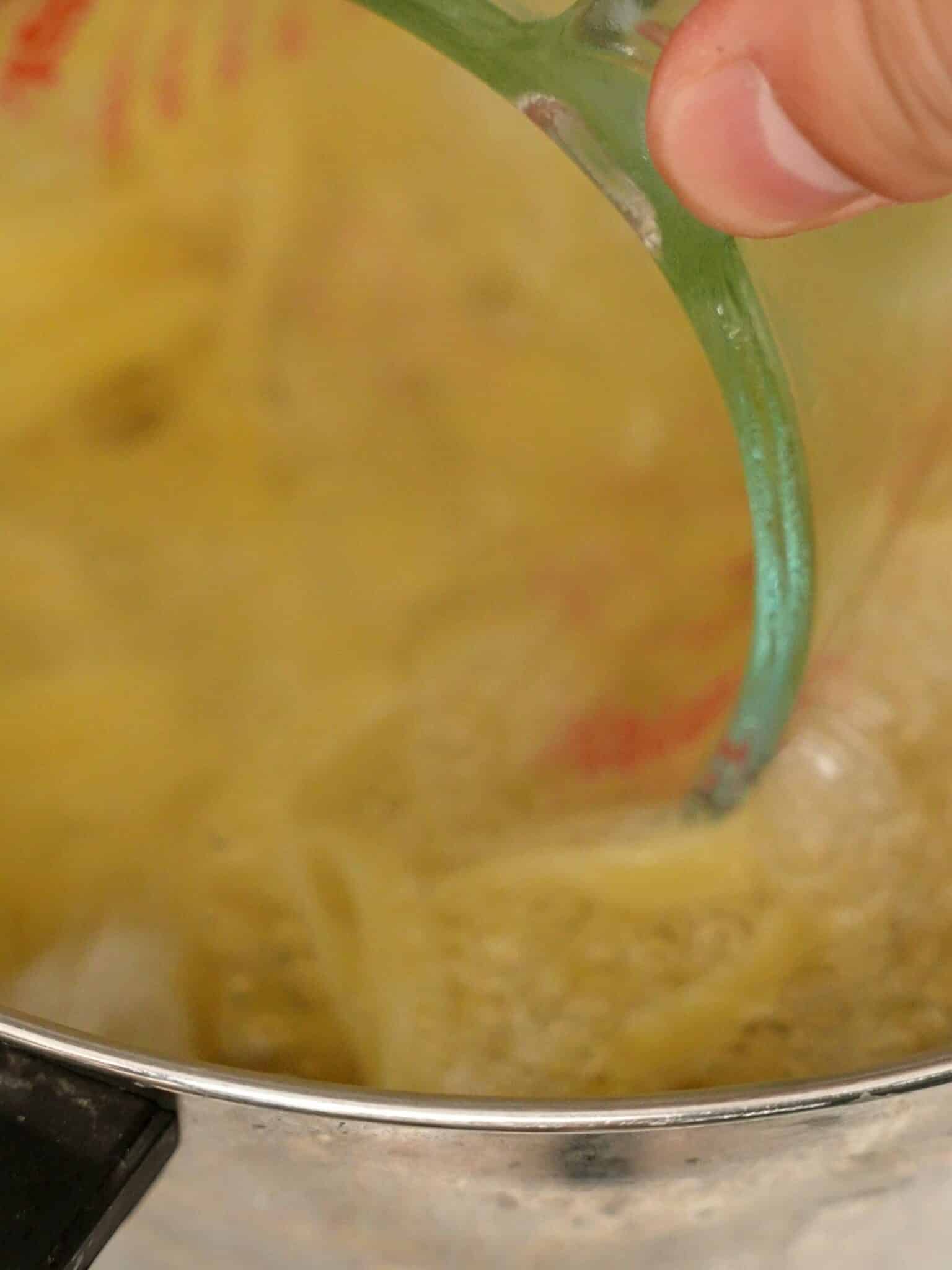 A measuring cup reserving pasta water from a pot.