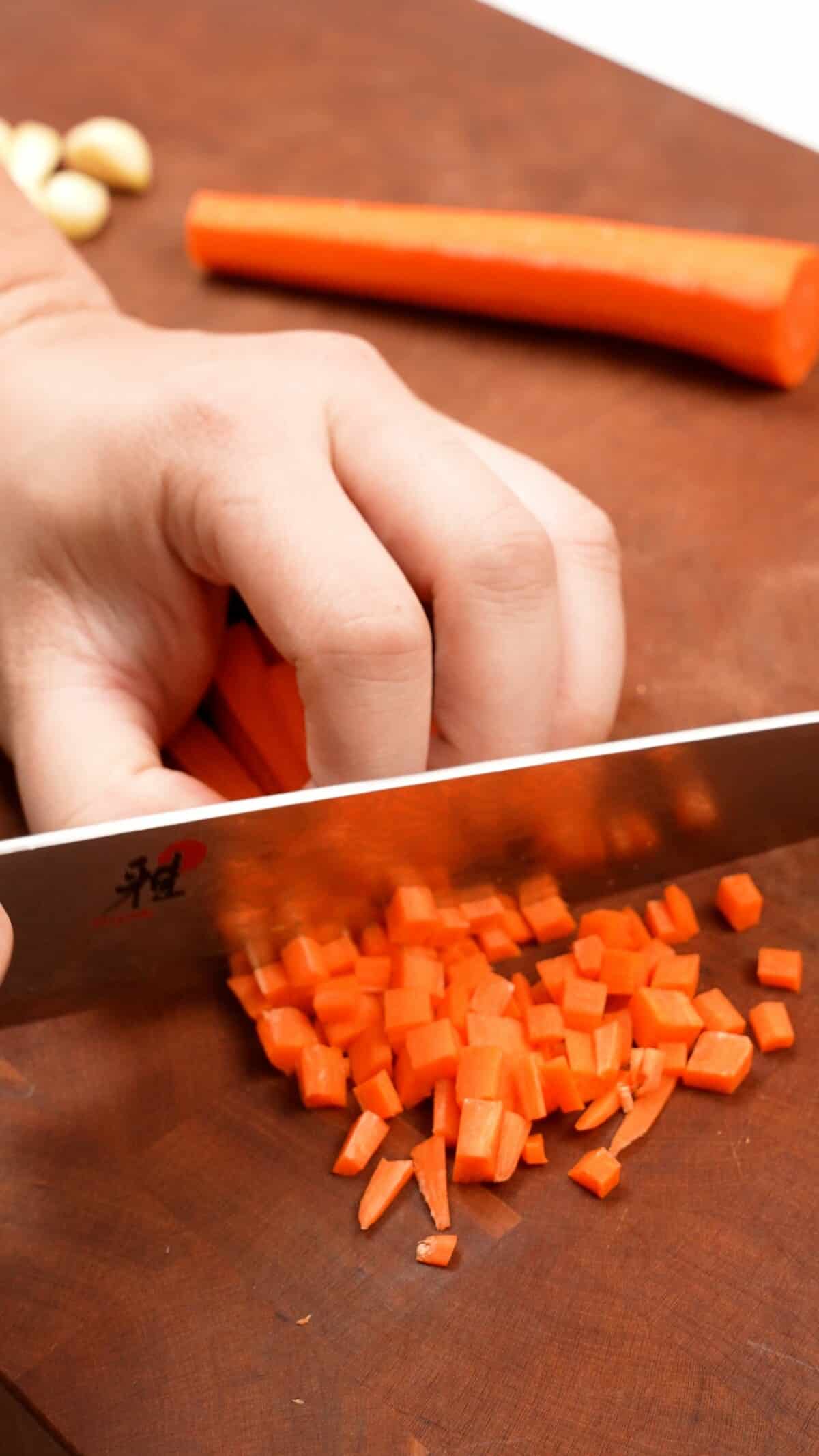 Cutting carrots into small pieces on a cutting board.