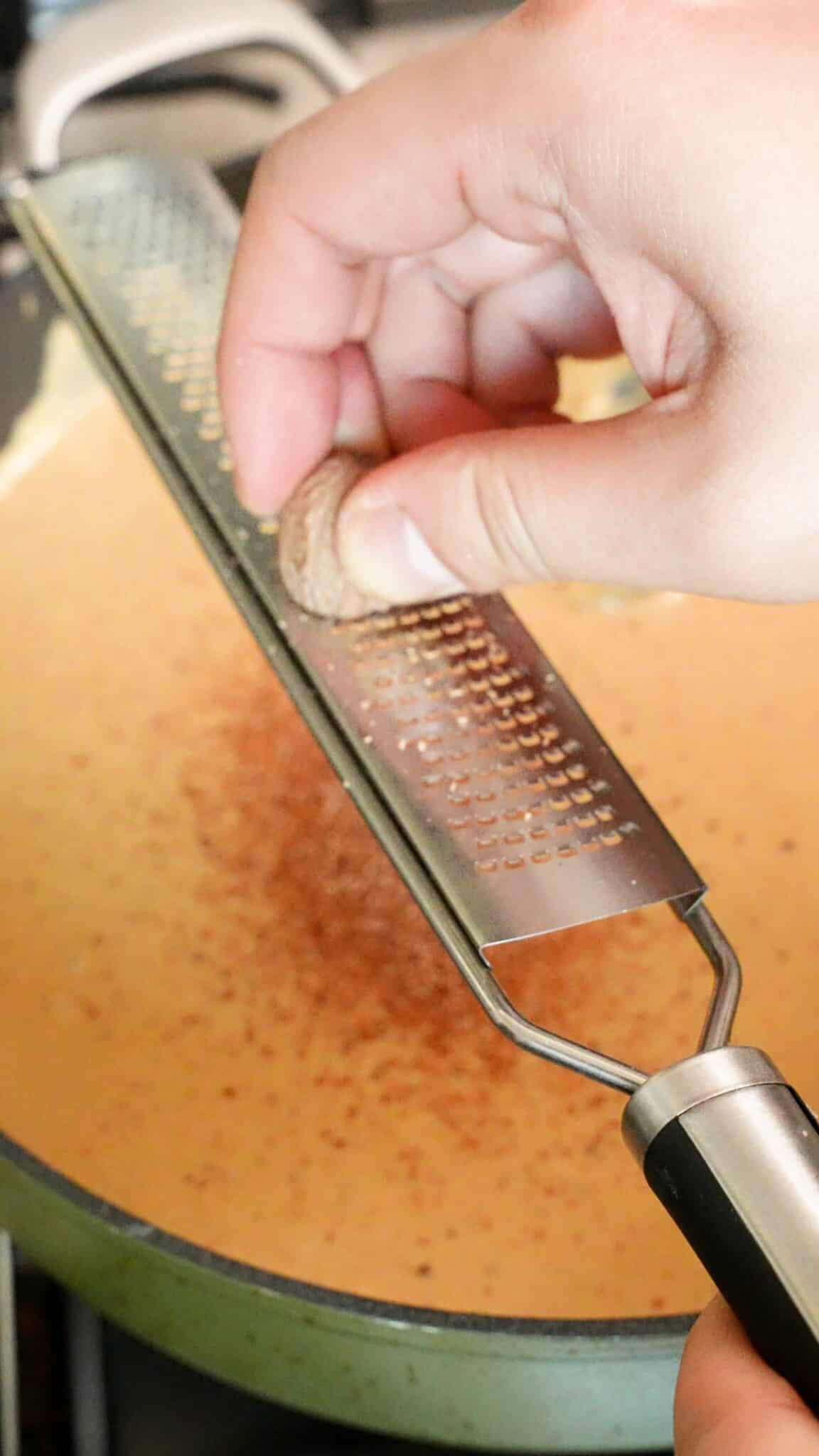 Grating nutmeg into the cheese sauce.