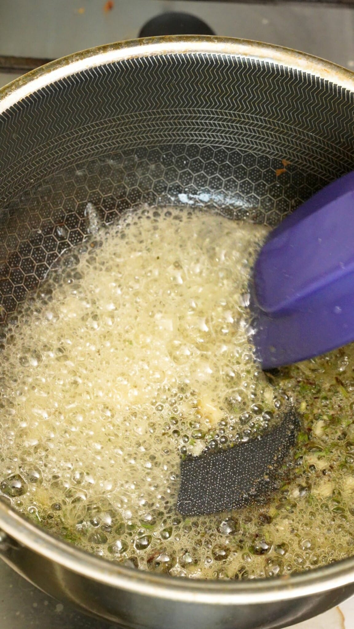 Garlic, fresh thyme and rosemary being sauteed in butter in a pot.