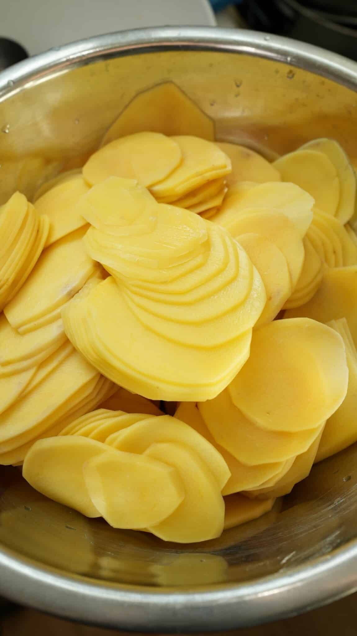 Thinly sliced potatoes in a metal bowl.