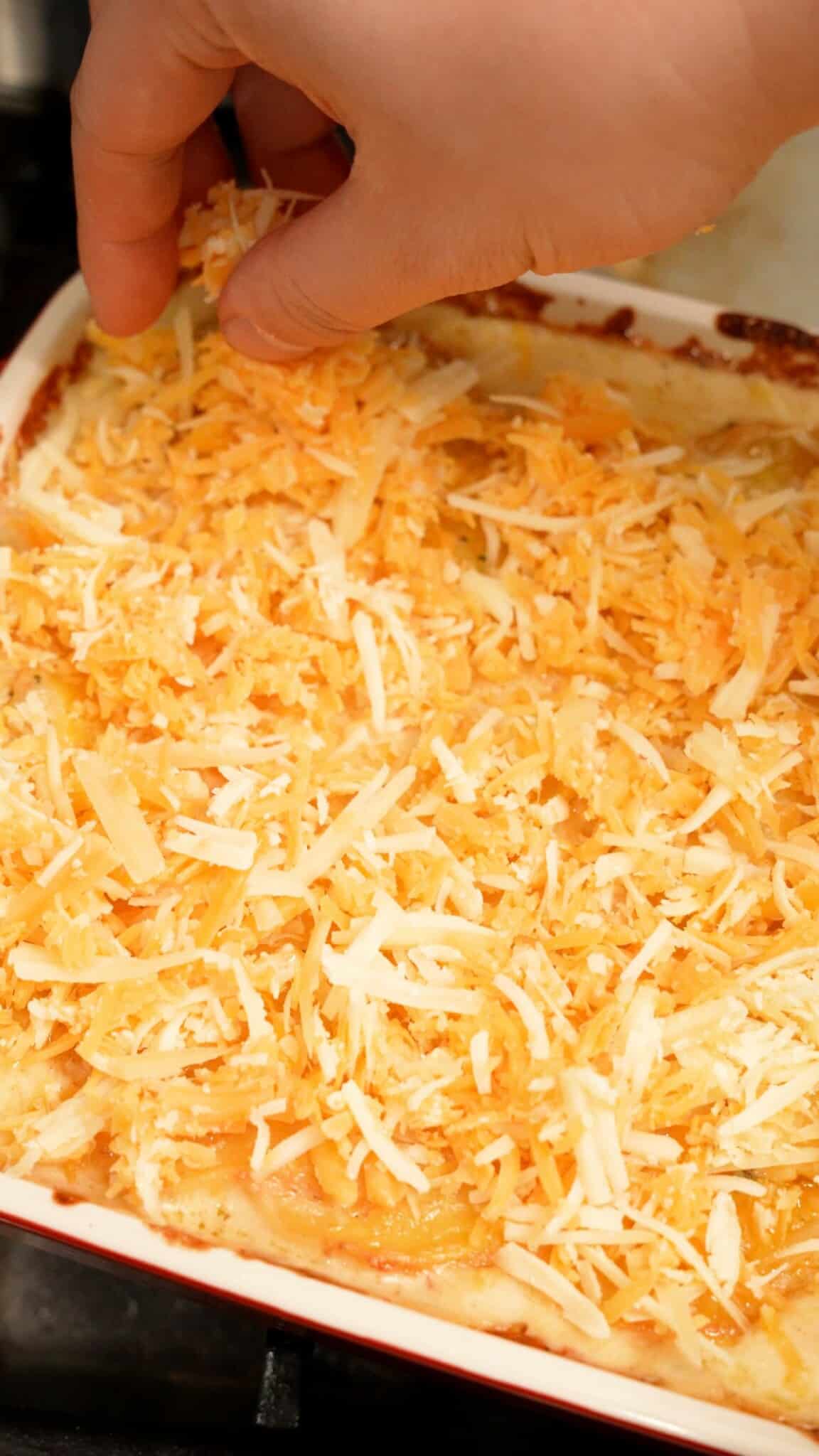 Cheese being topped over the baked potatoes au gratin to be placed in the oven.