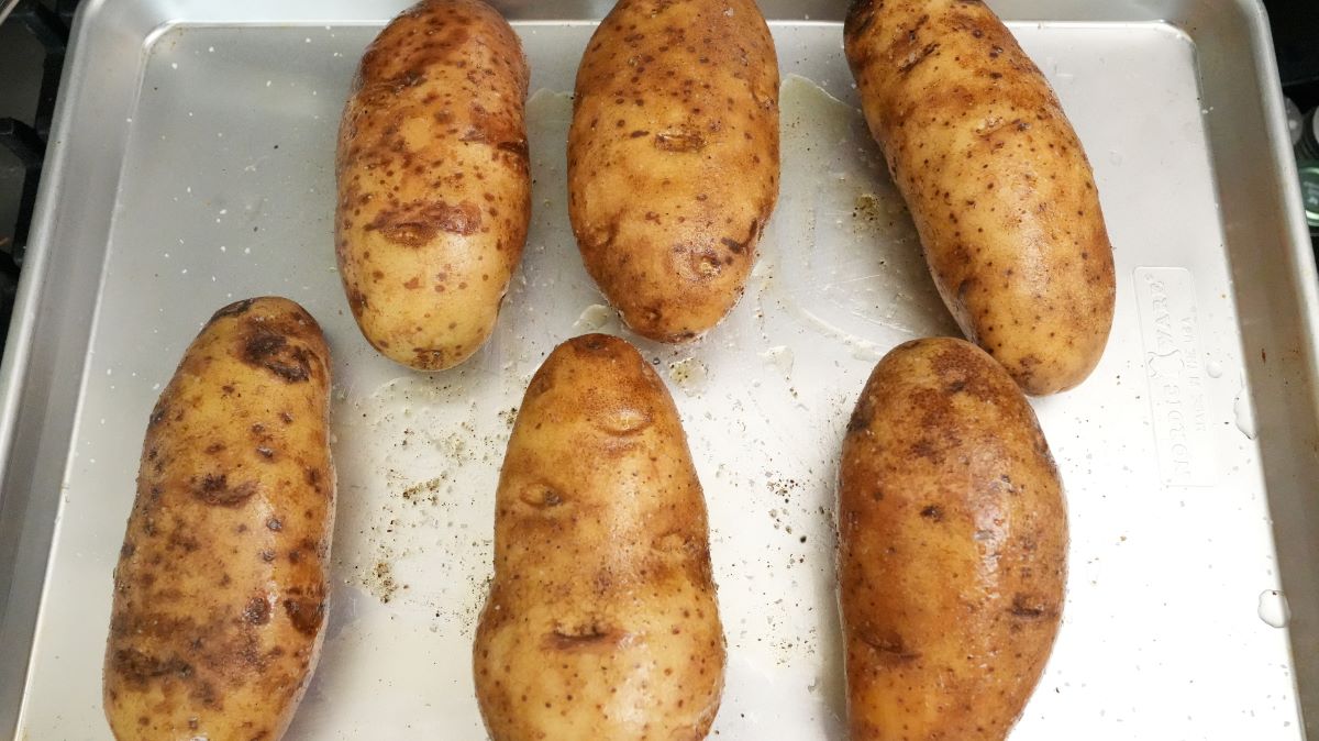 Russet potatoes on a baking sheet seasoned with salt and olive oil.