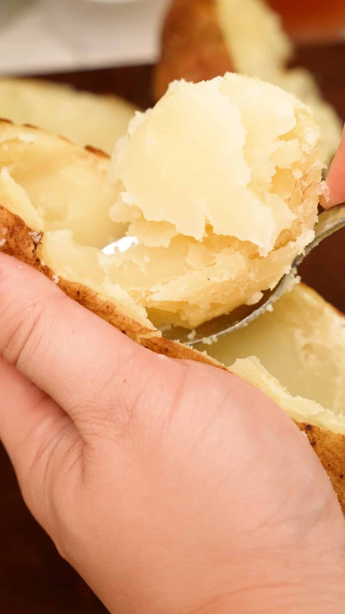 A hand scooping out the insides of the potato with a spoon.