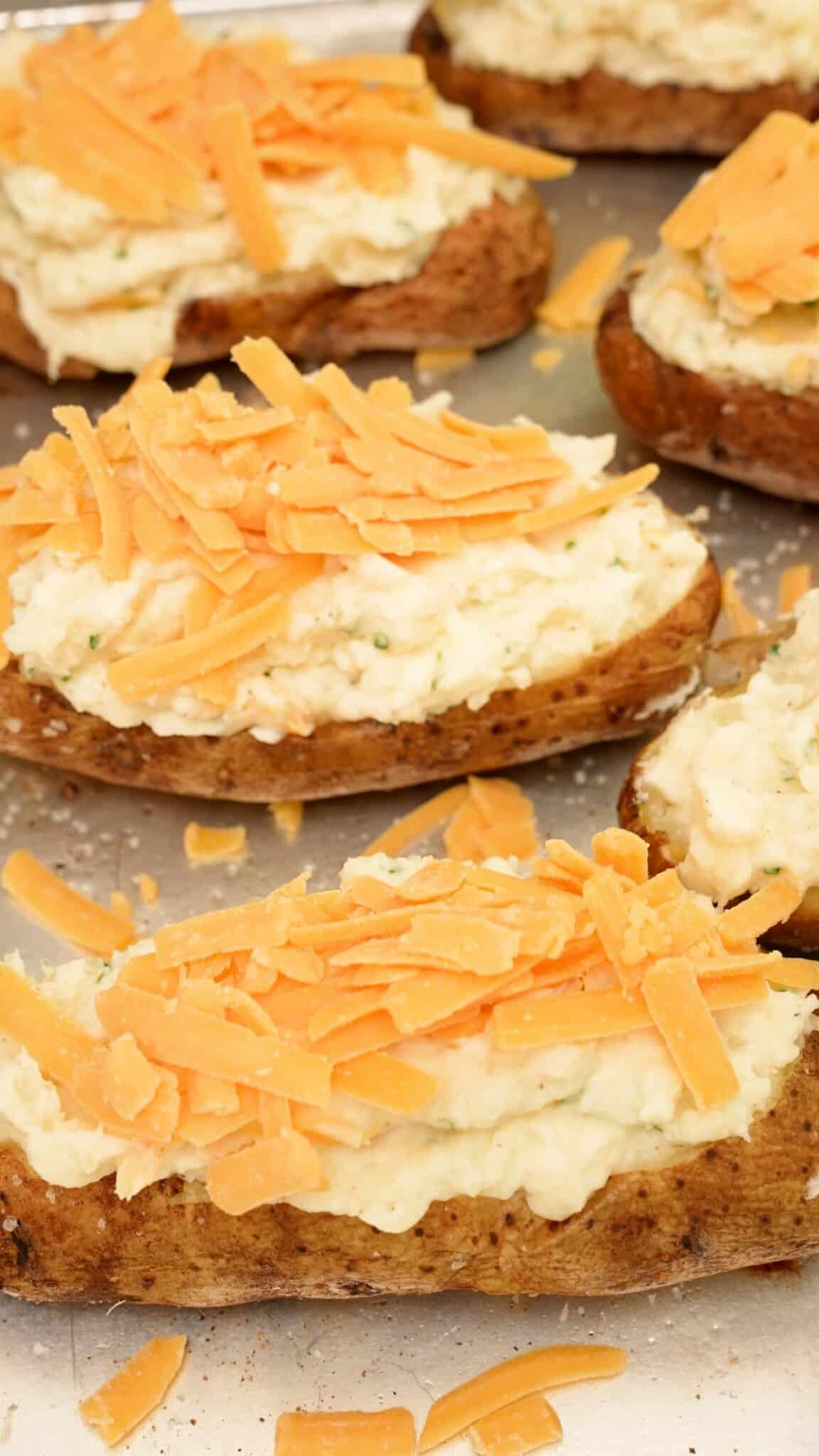 Twice baked potatoes topped with cheddar cheese on a baking sheet.