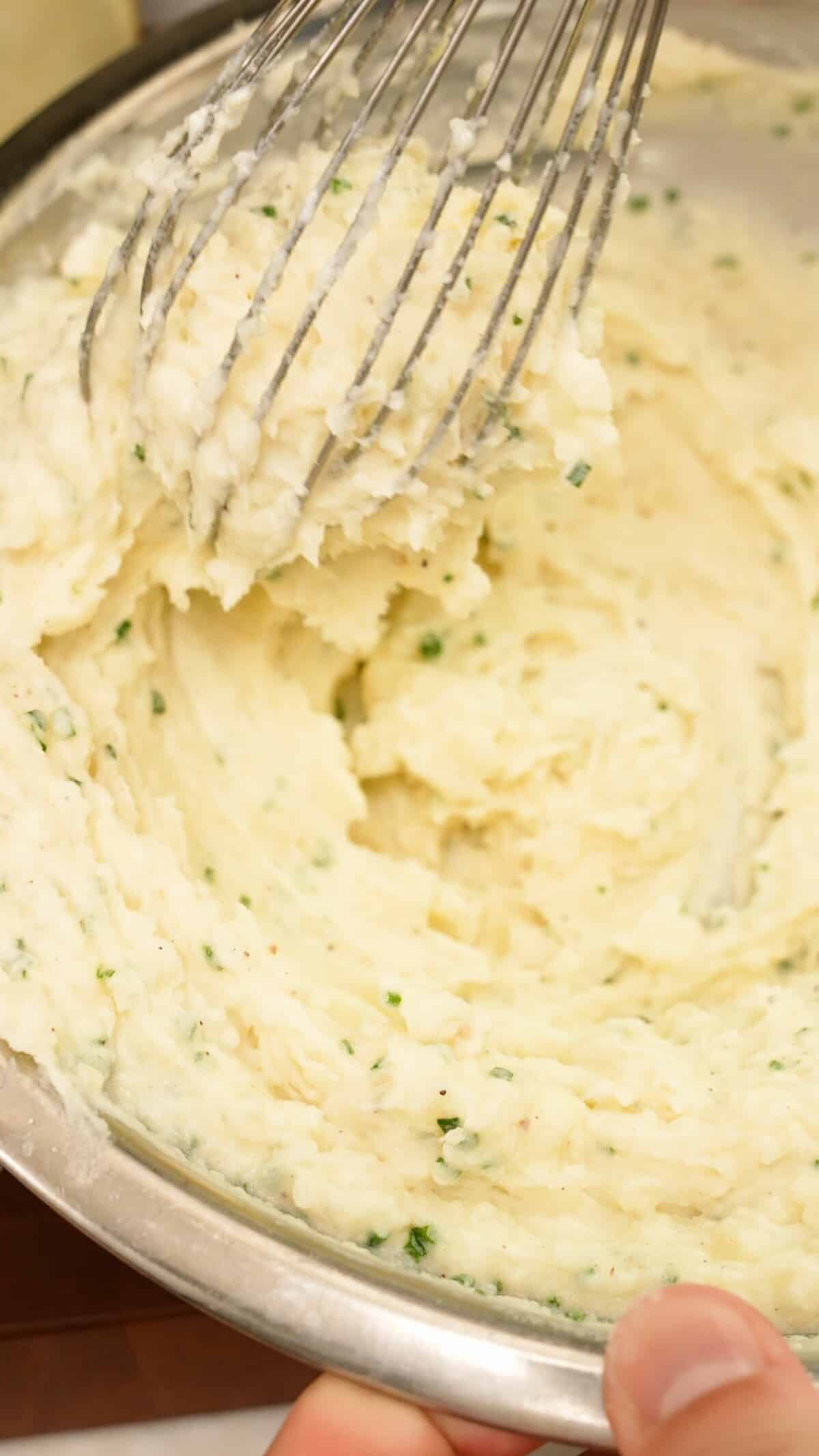 Whisking the potato filling for twice baked potatoes in a metal bowl.