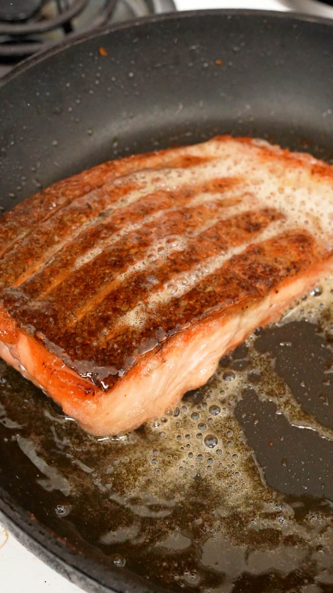 A salmon skin being basted with oil in a pan.