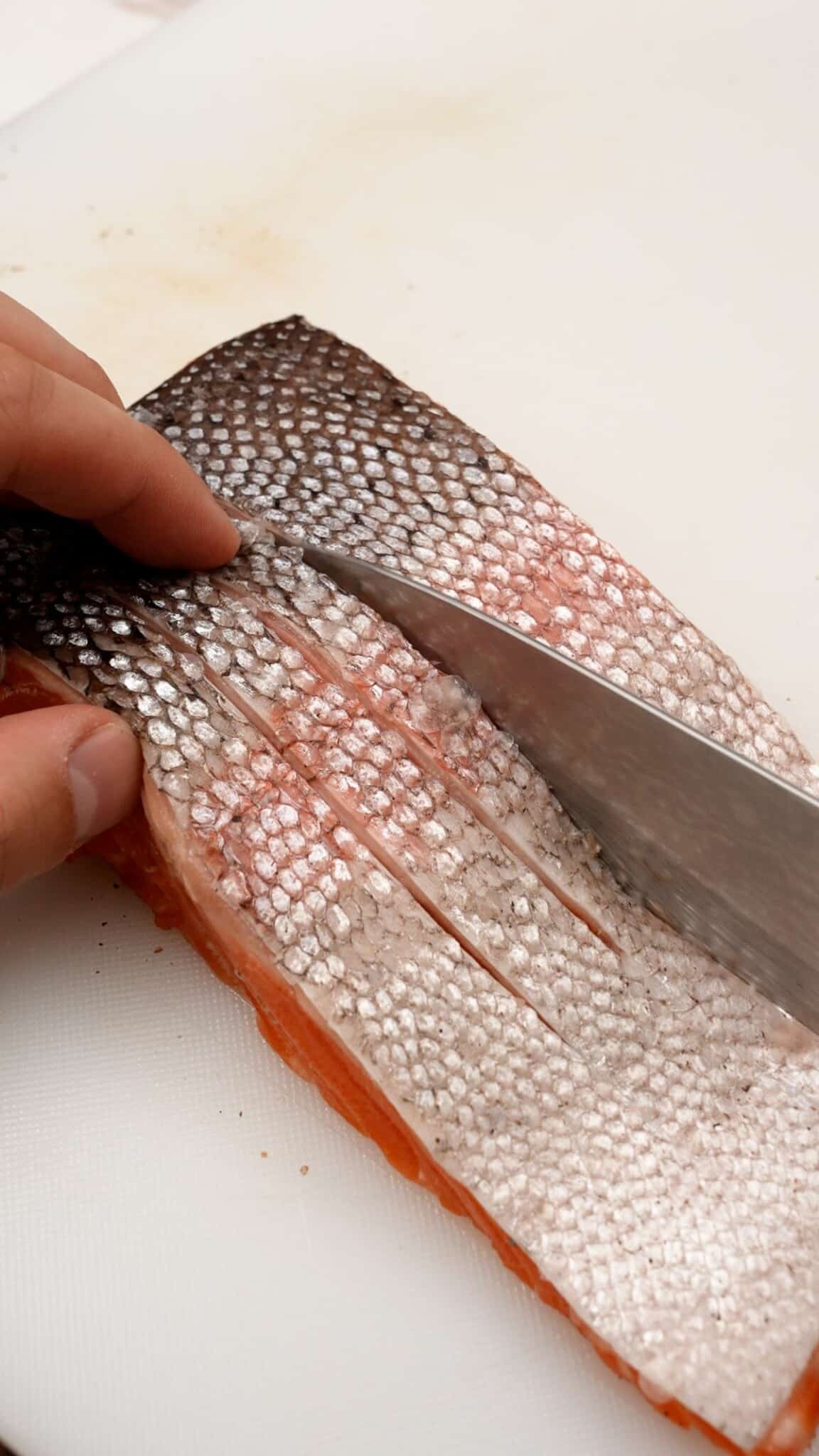 A knife making vertical cuts through salmon skin.