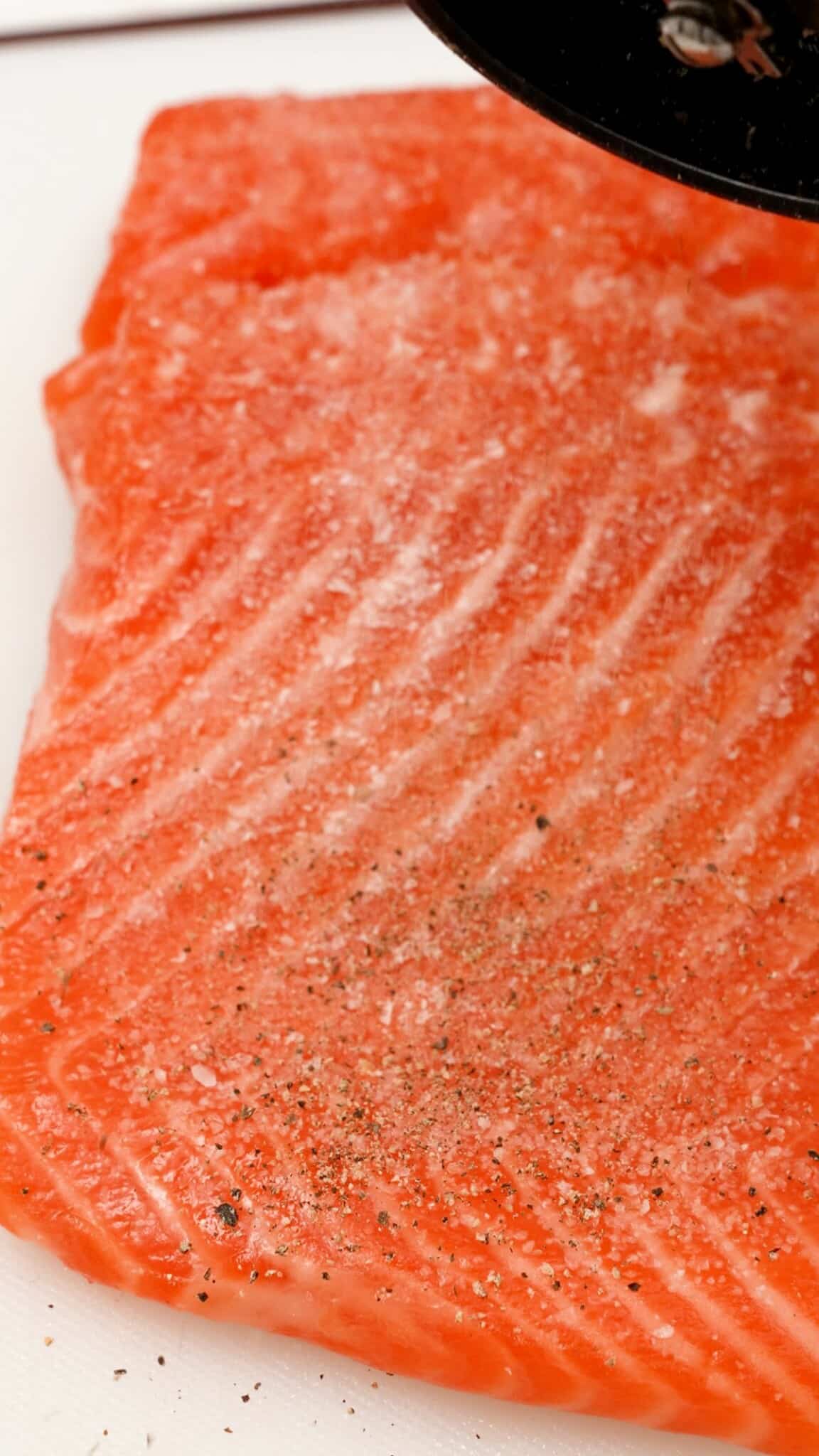 The flesh side of a salmon filet seasoned with salt and pepper.