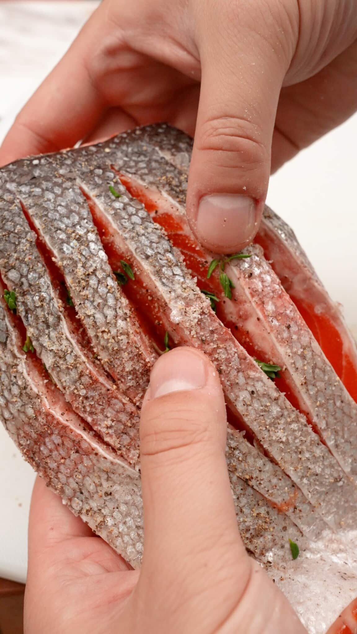 Two hands holding a salmon filet that's seasoned inside cuts on the skin.