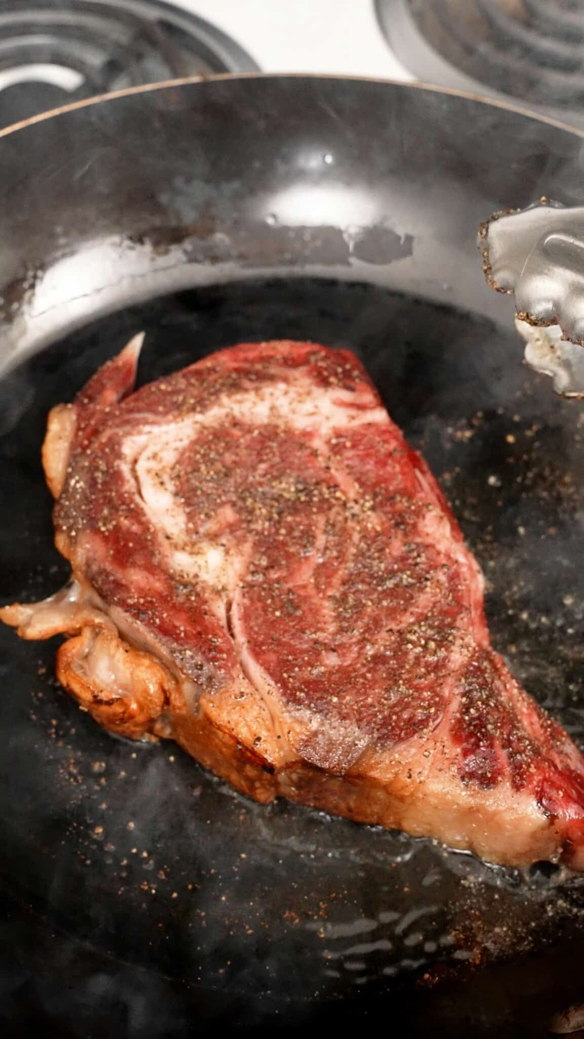 Steak searing in a carbon steel pan.