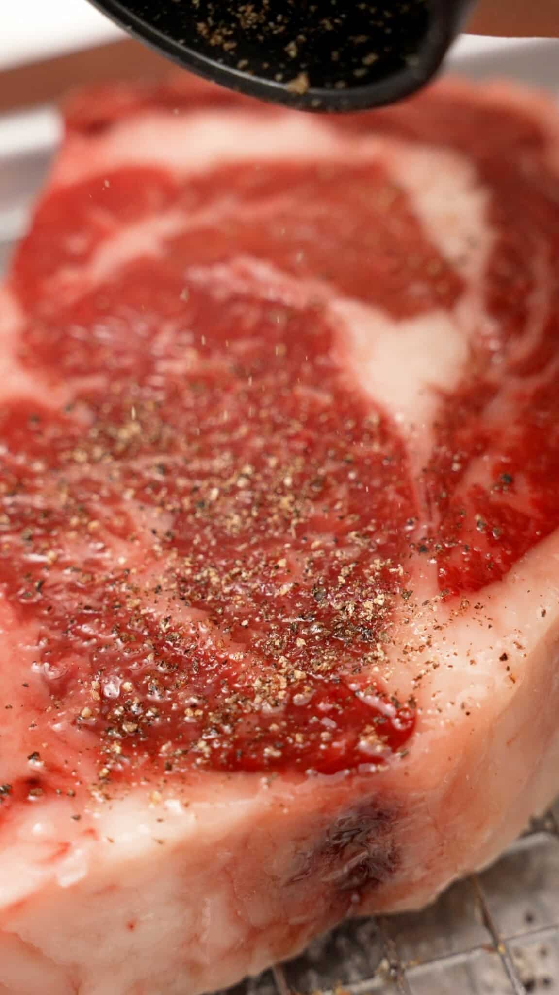 A steak being seasoned with black pepper.