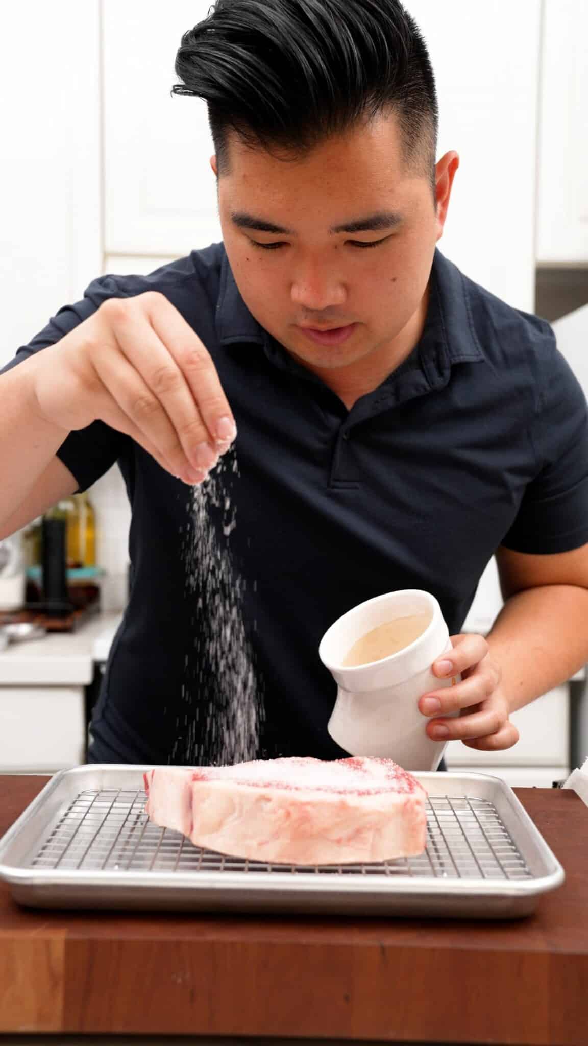 A man seasoning steak with kosher salt.