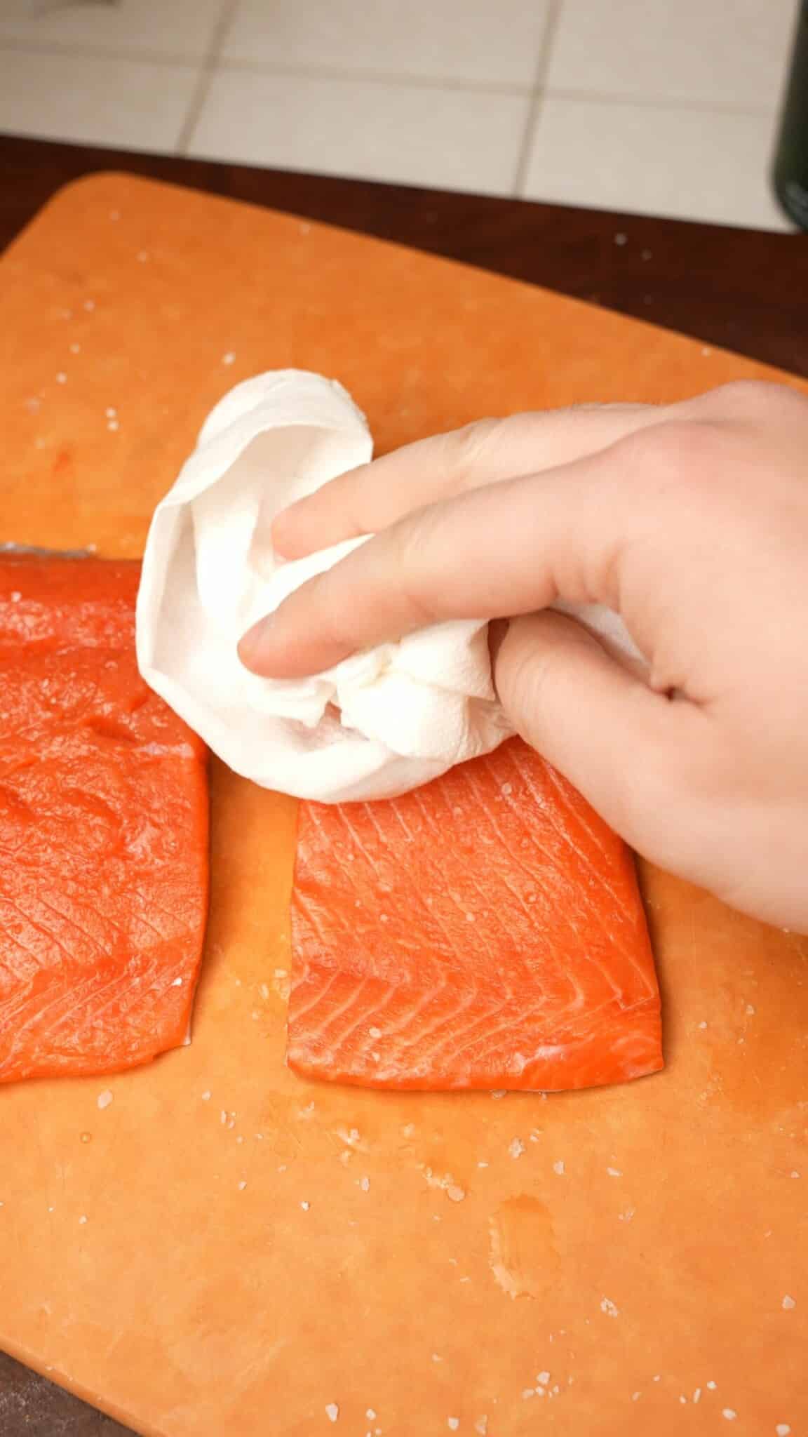 Patting salmon with a paper towel to remove excess water.