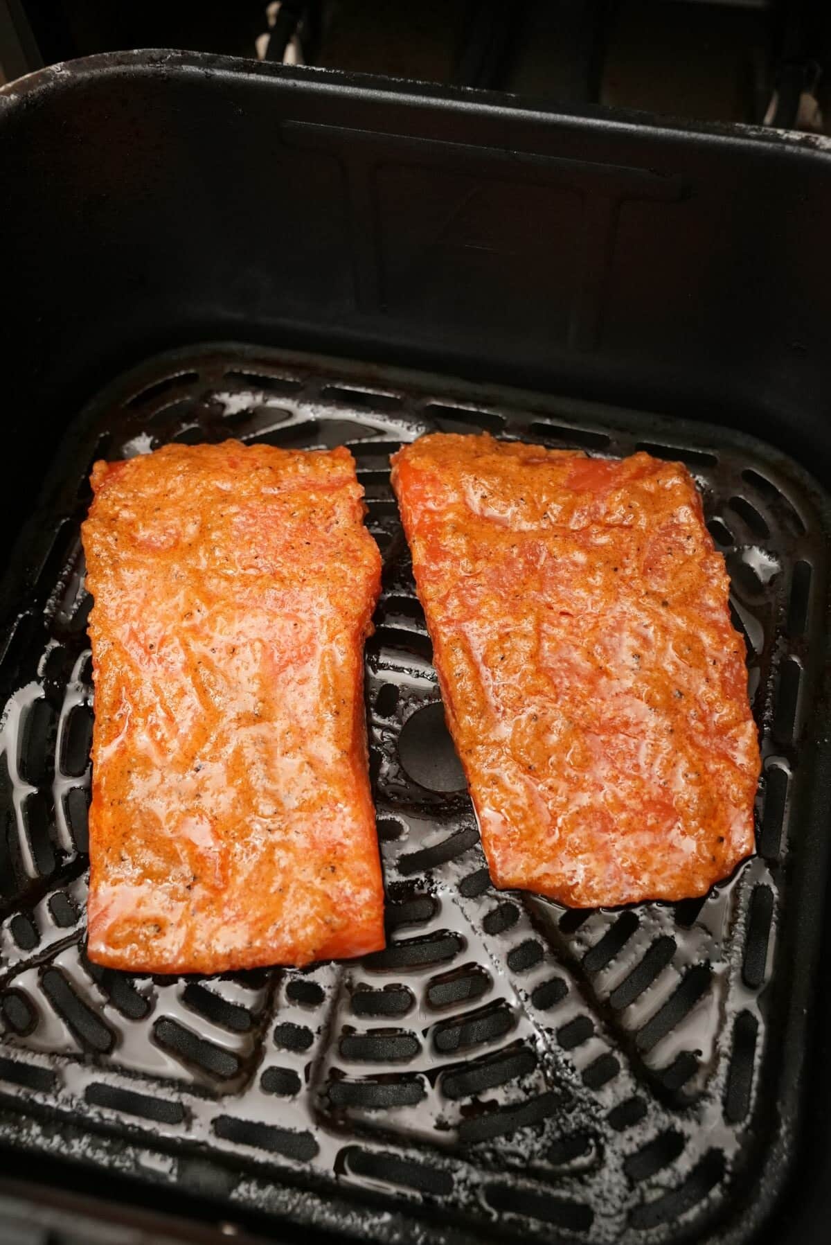 Two uncooked salmon filets on an oiled air fryer basket.