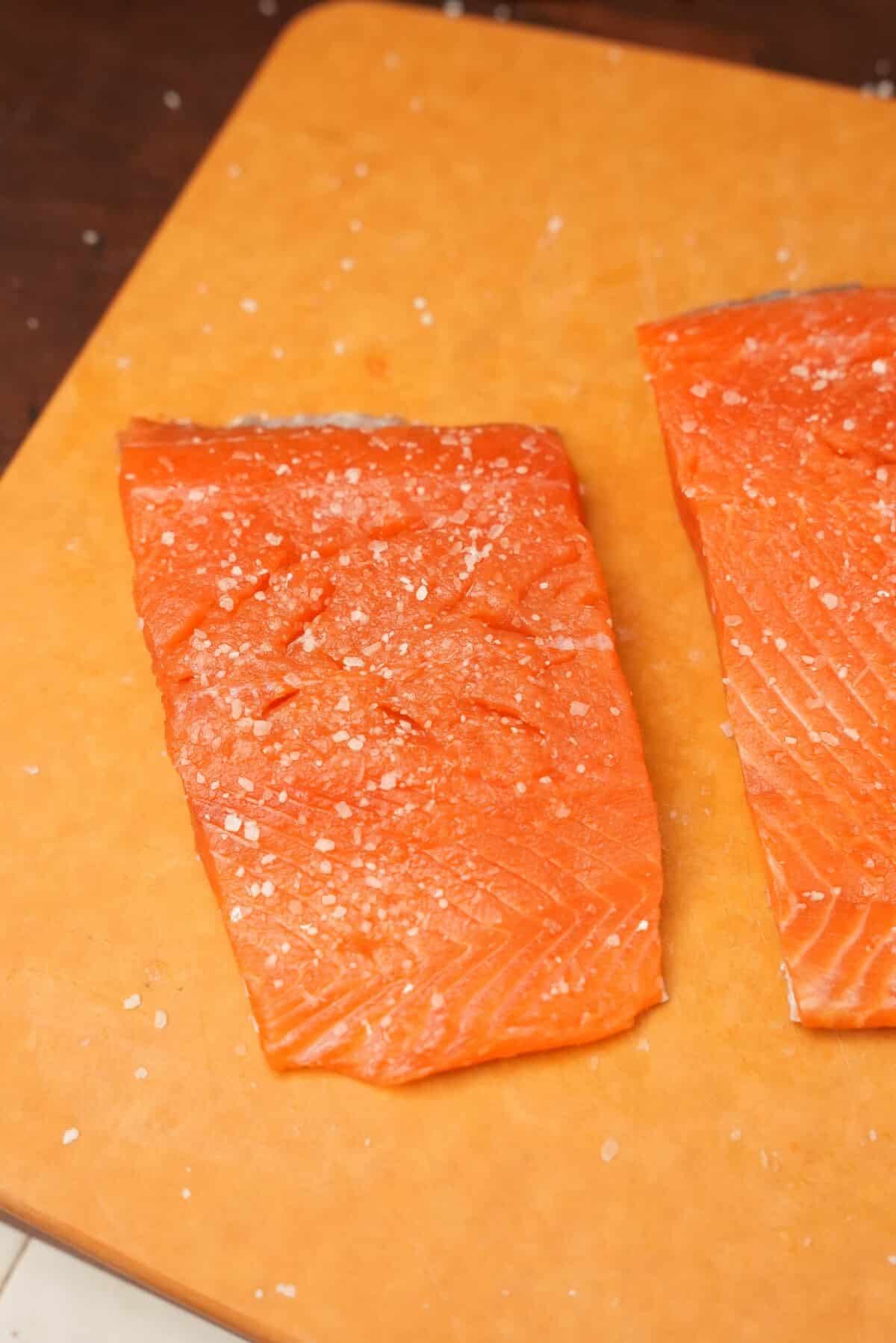 Salmon filets on a cutting board seasoned with salt.