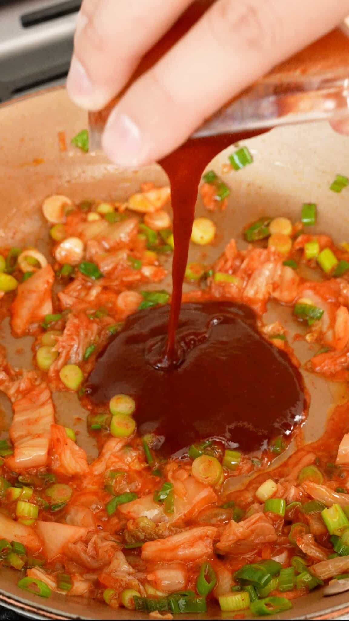 Adding gochujang sauce to the pan with scallions and kimchi.