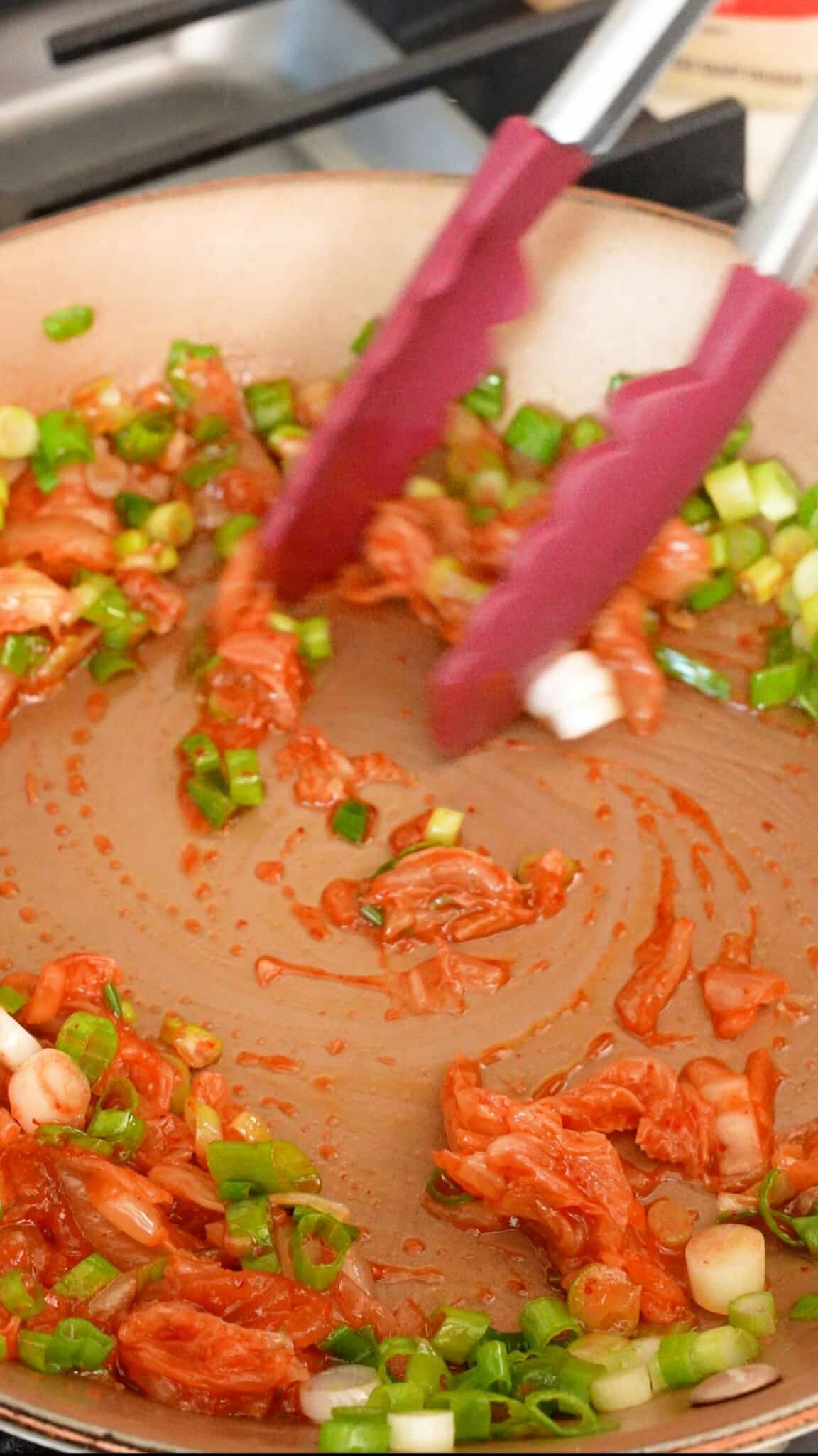 Cooking kimchi and scallions in a pan.