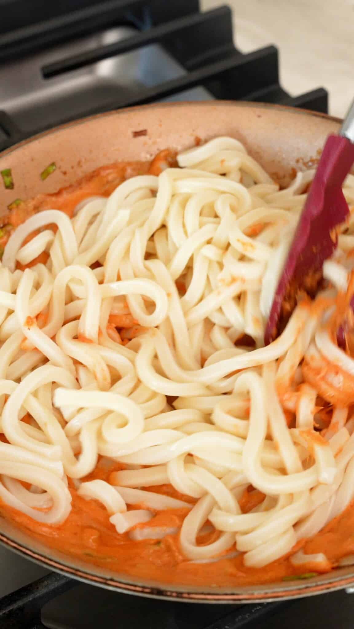 Adding cooked udon noodles to the pan.