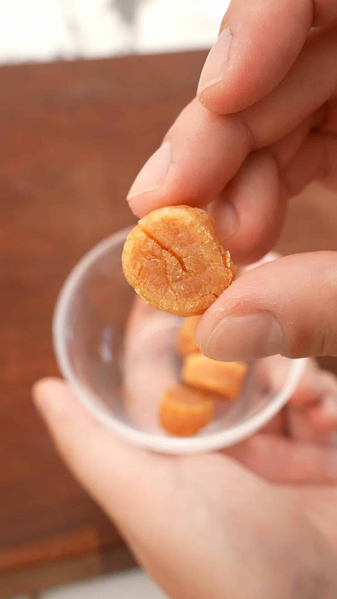 A piece of dried scallop being held by a hand.