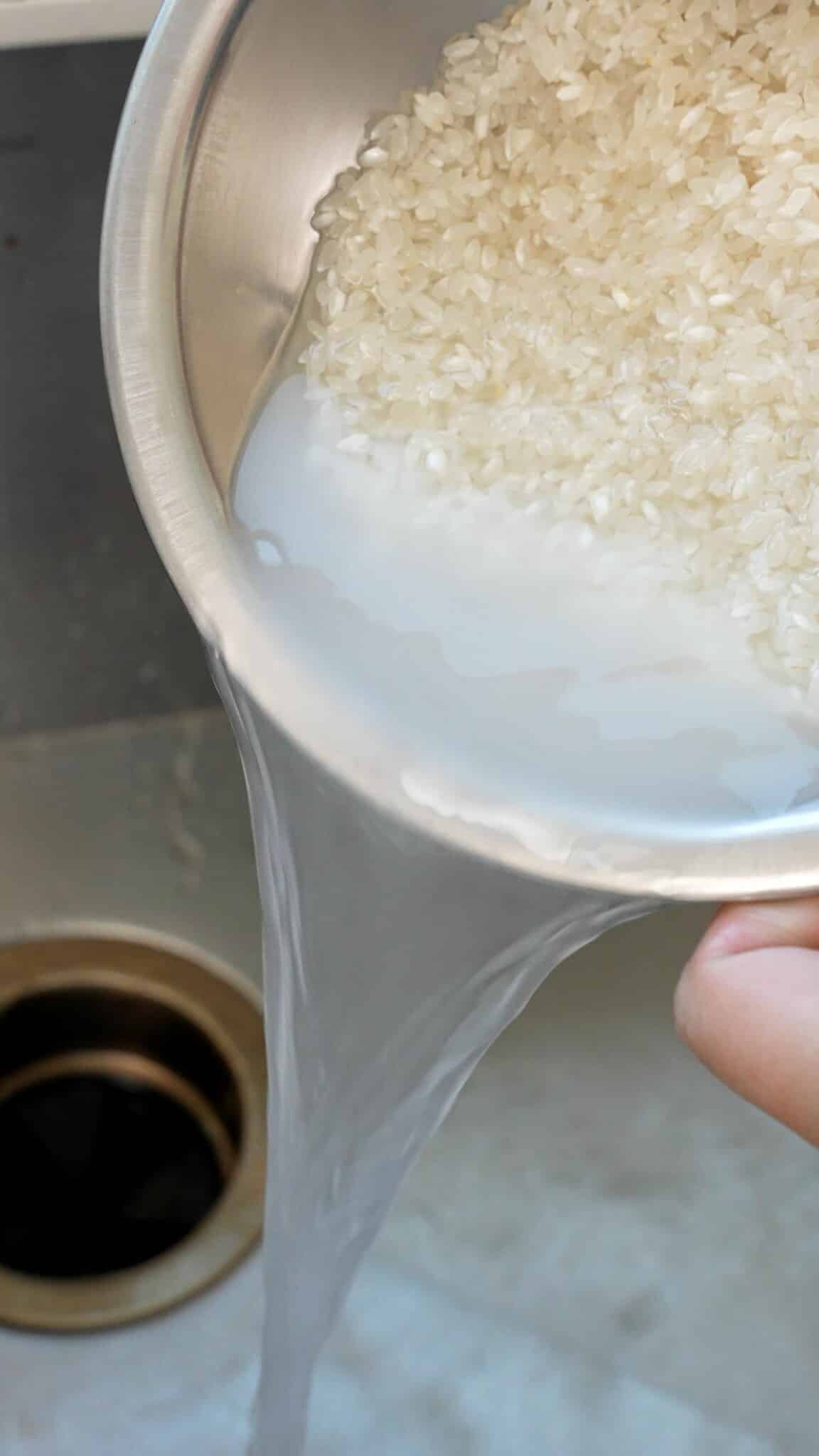 White rice being washed with water over a sink.