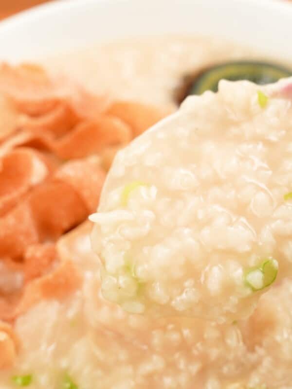 A spoon with congee and toppings in a bowl.