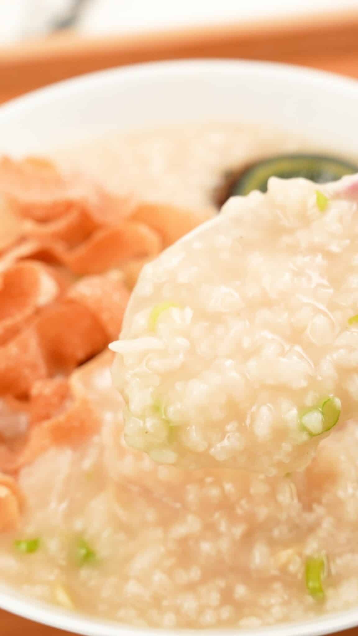 A spoon with congee and toppings in a bowl.