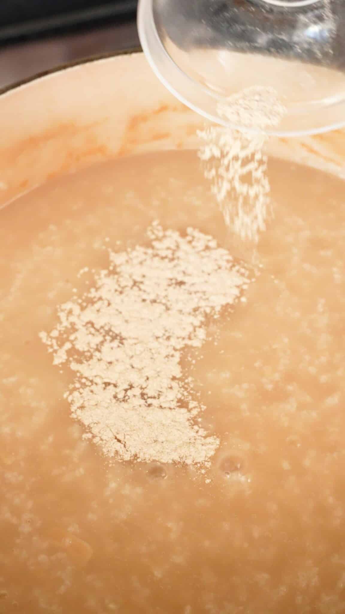 Cooked congee being seasoned with white pepper in a pot.