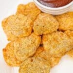 Air fryer chicken nuggets on a plate with BBQ sauce.