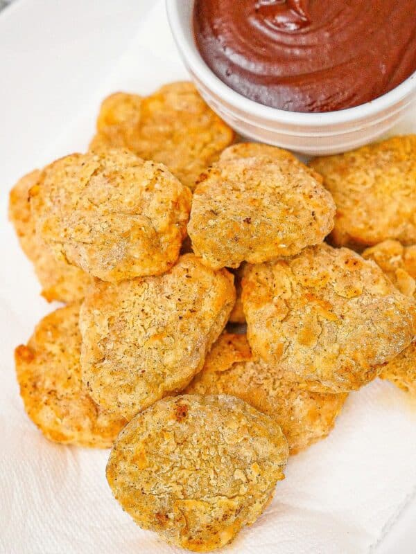 Air fryer chicken nuggets on a plate with BBQ sauce.