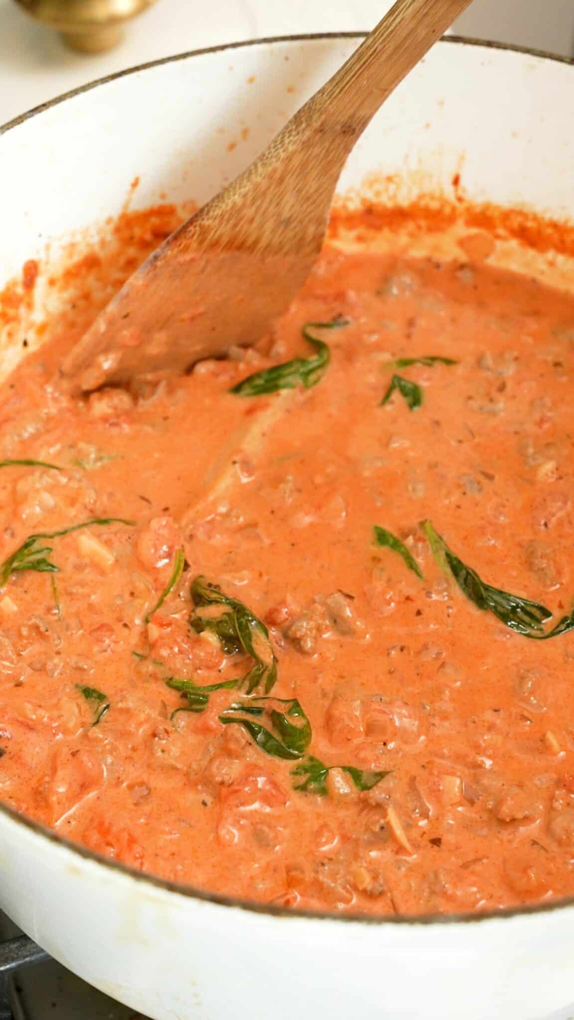 A wooden spatula mixing the pasta sauce in a pot.