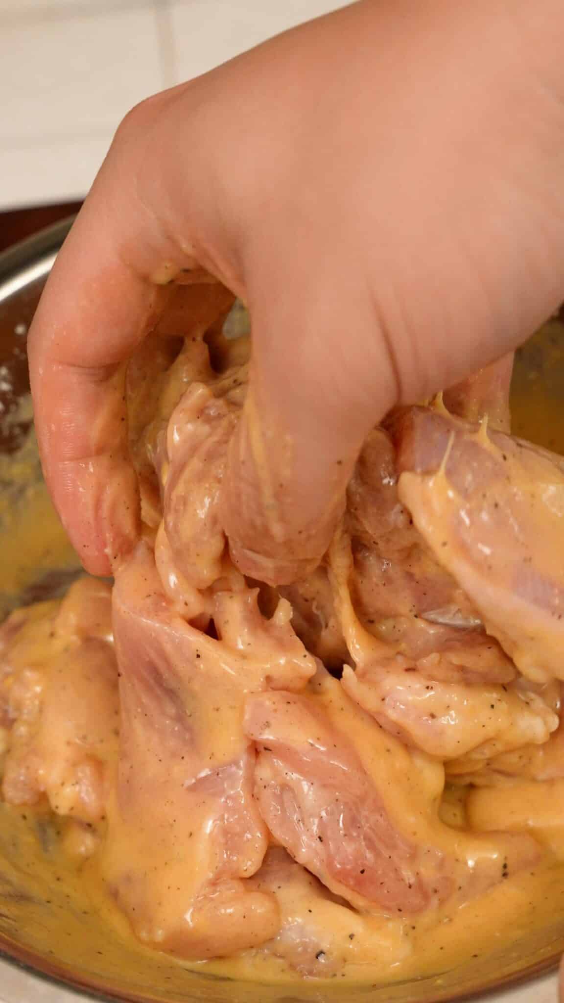 A hand mixing chicken katsu sliders in wet batter.