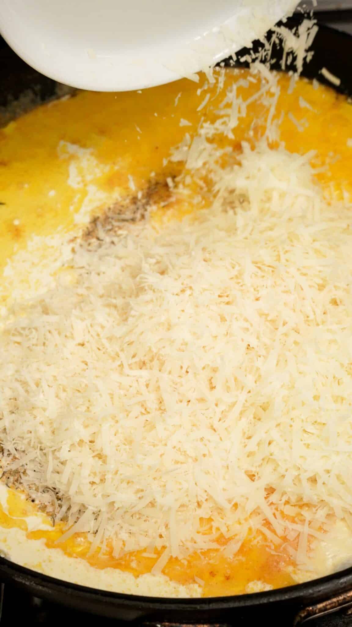 Parmesan and pecorino romano cheese being added to alfredo sauce.