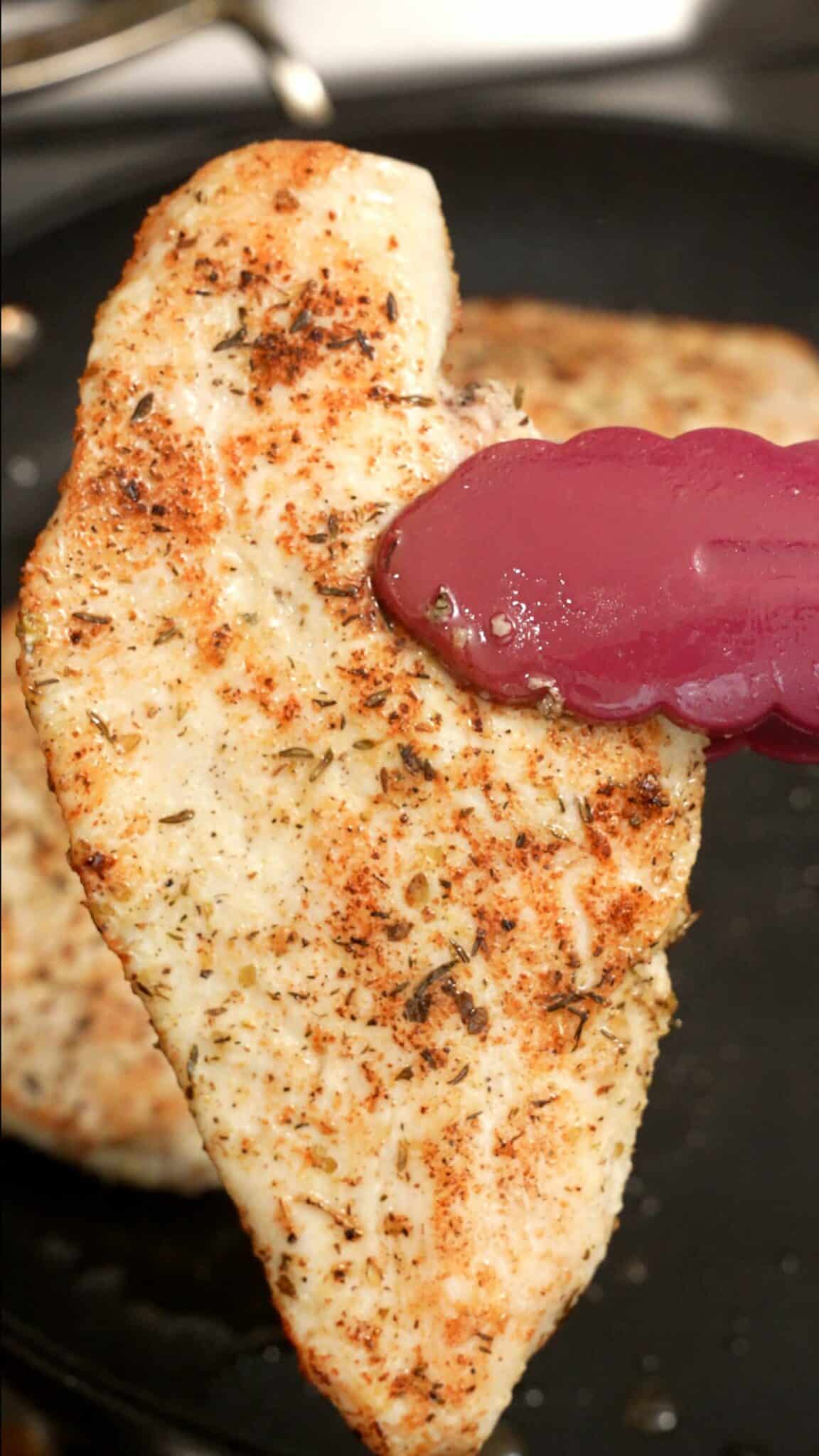 Seared cooked chicken breasts held by a pair of tongs.