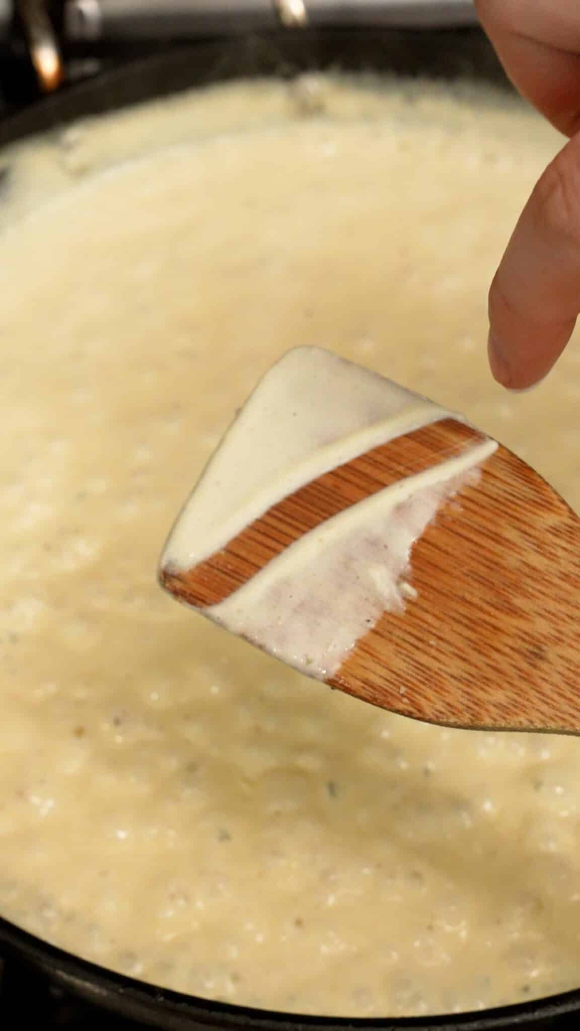 A wooden spoon showing the thickeness of the alfredo sauce.