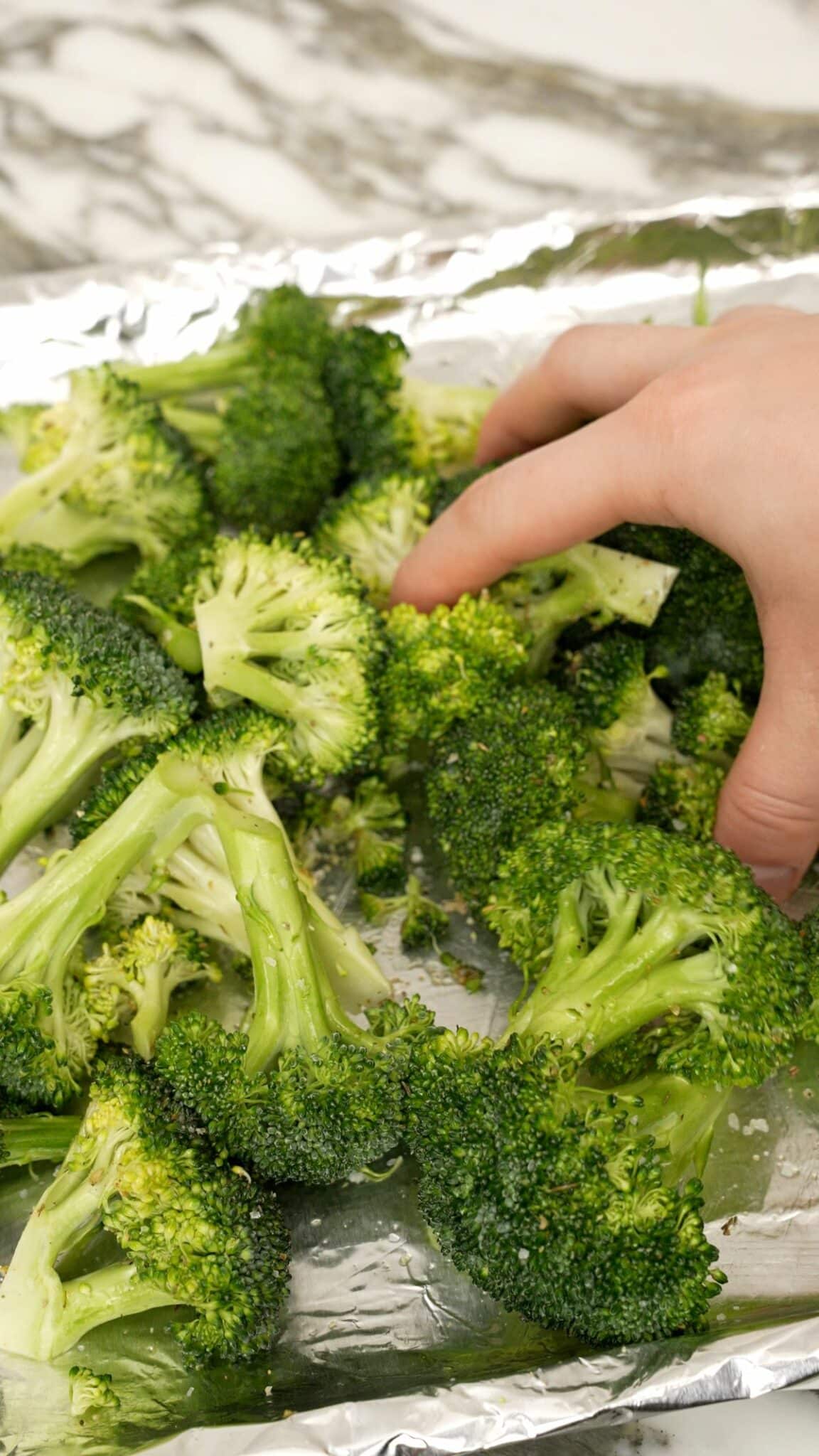 A hand mixing seasoned broccoli for Chicken and Broccoli Fettuccine Alfredo.