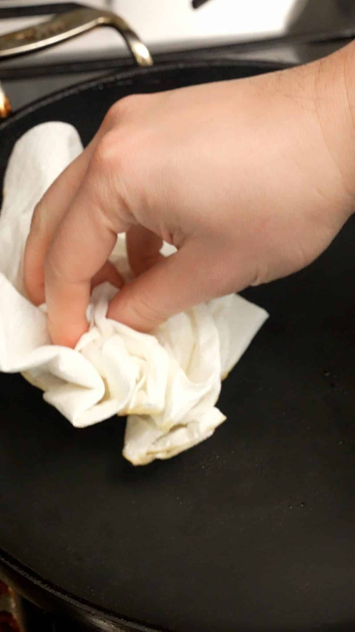 A hand wiping out the nonstick pan with a paper towel.