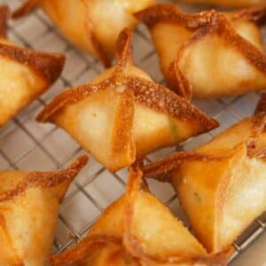 Crab rangoons resting on a wire rack after frying.