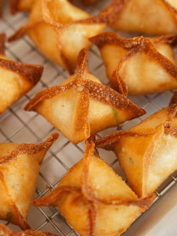 Crab rangoons resting on a wire rack after frying.